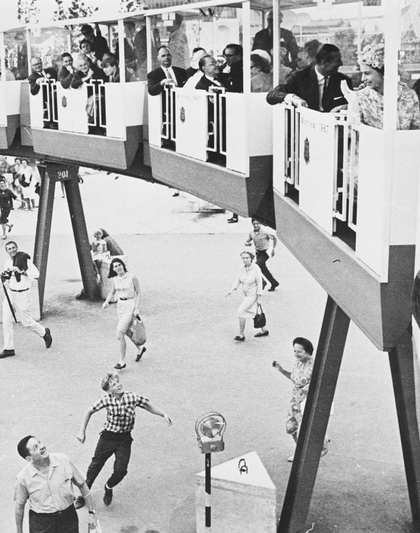 Photograph of HM Queen Elizabeth II waving from a car on a monorail sightseeing train at EXPO '67 in Montreal, Canada. Seated behind the Queen can be seen Prince Philip, Duke of Edinburgh.