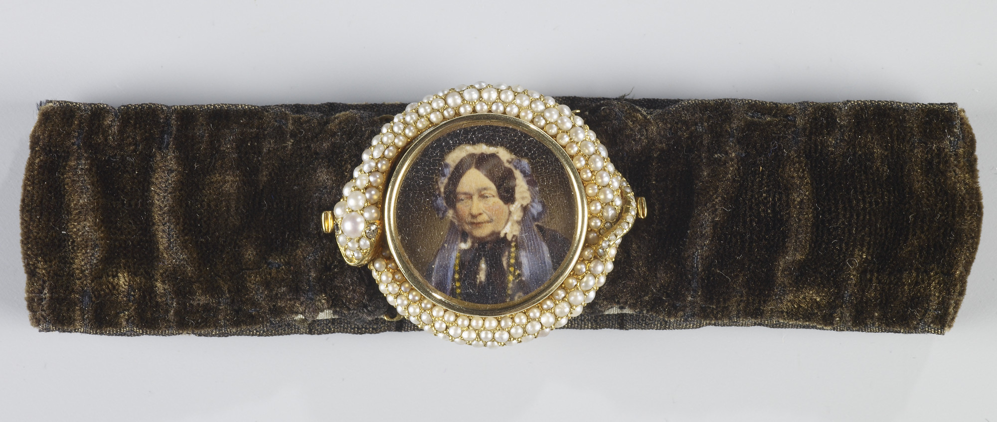 Velvet bracelet with pearl ouroboros, an ancient symbol of a serpent eating their own tail,&nbsp;surrounding a&nbsp;miniature of&nbsp;Princess Victoria,&nbsp;Duchess of Kent. She is shown&nbsp;bust-length against a grey background. Her head is turned half