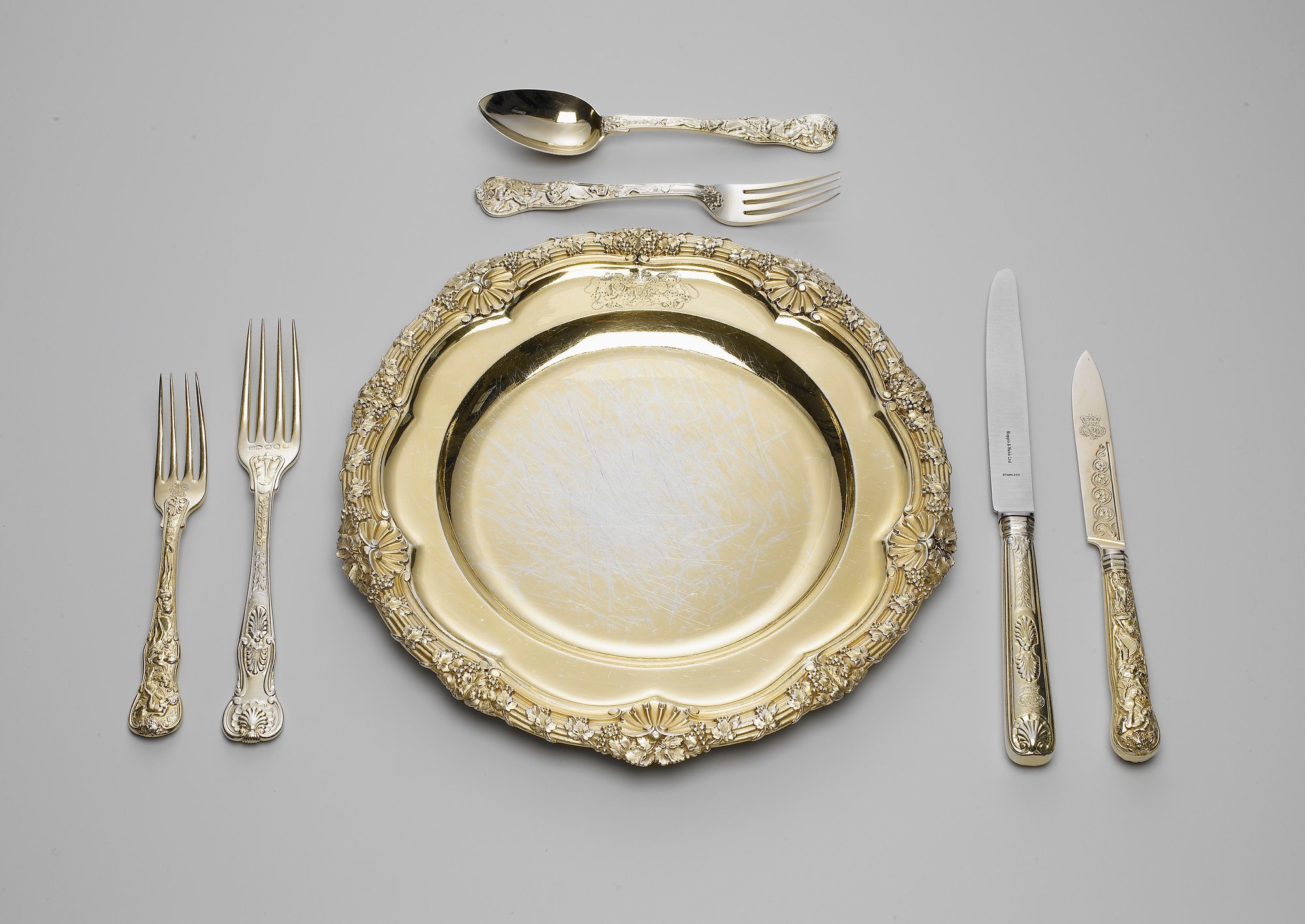 A set of silver-gilt plates; the reeded rim cast with fruiting vines and scallop shells. The plate is engraved with the Royal coat of arms, with supporters, mantling and coronet.