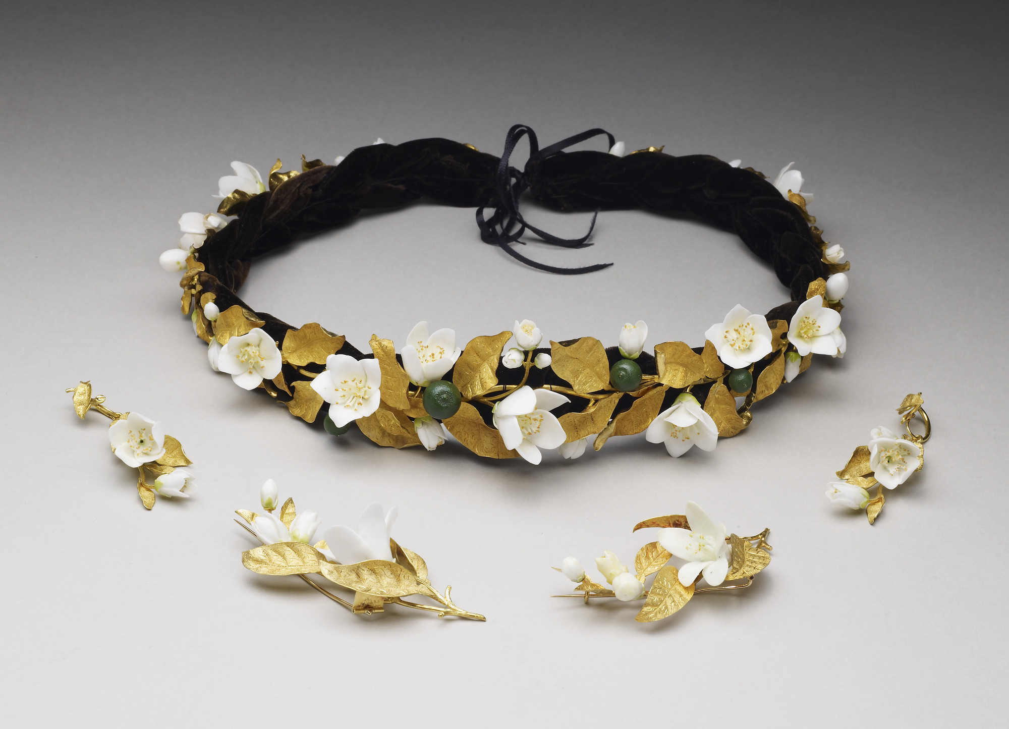 Headdress in the form of a wreath of orange blossoms with gold leaves, white porcelain flowers and green enamelled oranges. Black plaited velvet band, and silk ribbon.
Within the language of flowers, one remarkably consistent usage was the symbolic meani