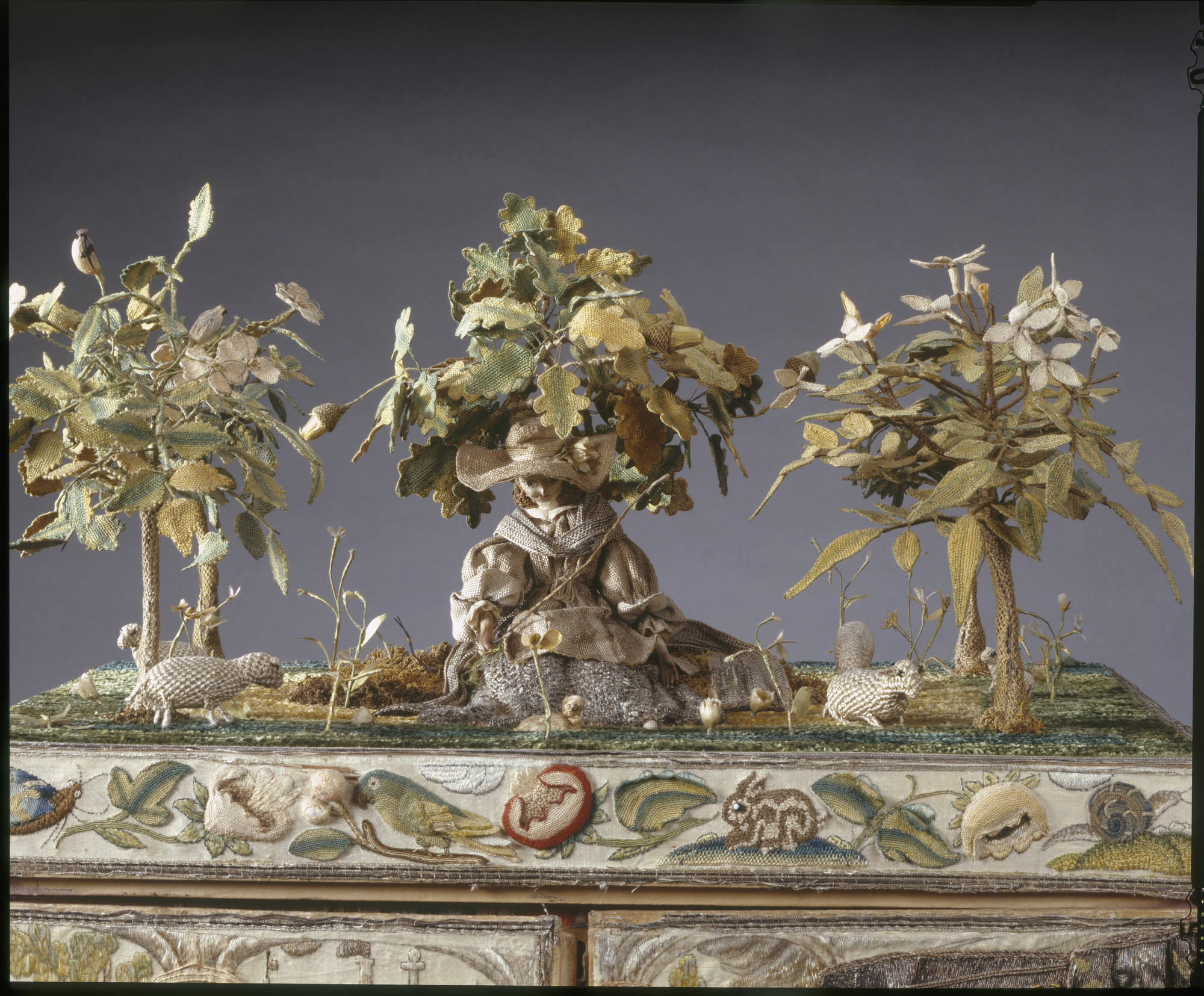 A stumpwork casket with two doors and brass drop handles and interior fitted with mirror and small drawers.Top decorated with shepherdess wearing a hat with four sheep, a lamb and a dog, sitting under an oak tree. 
Embroidered caskets decorated with raise
