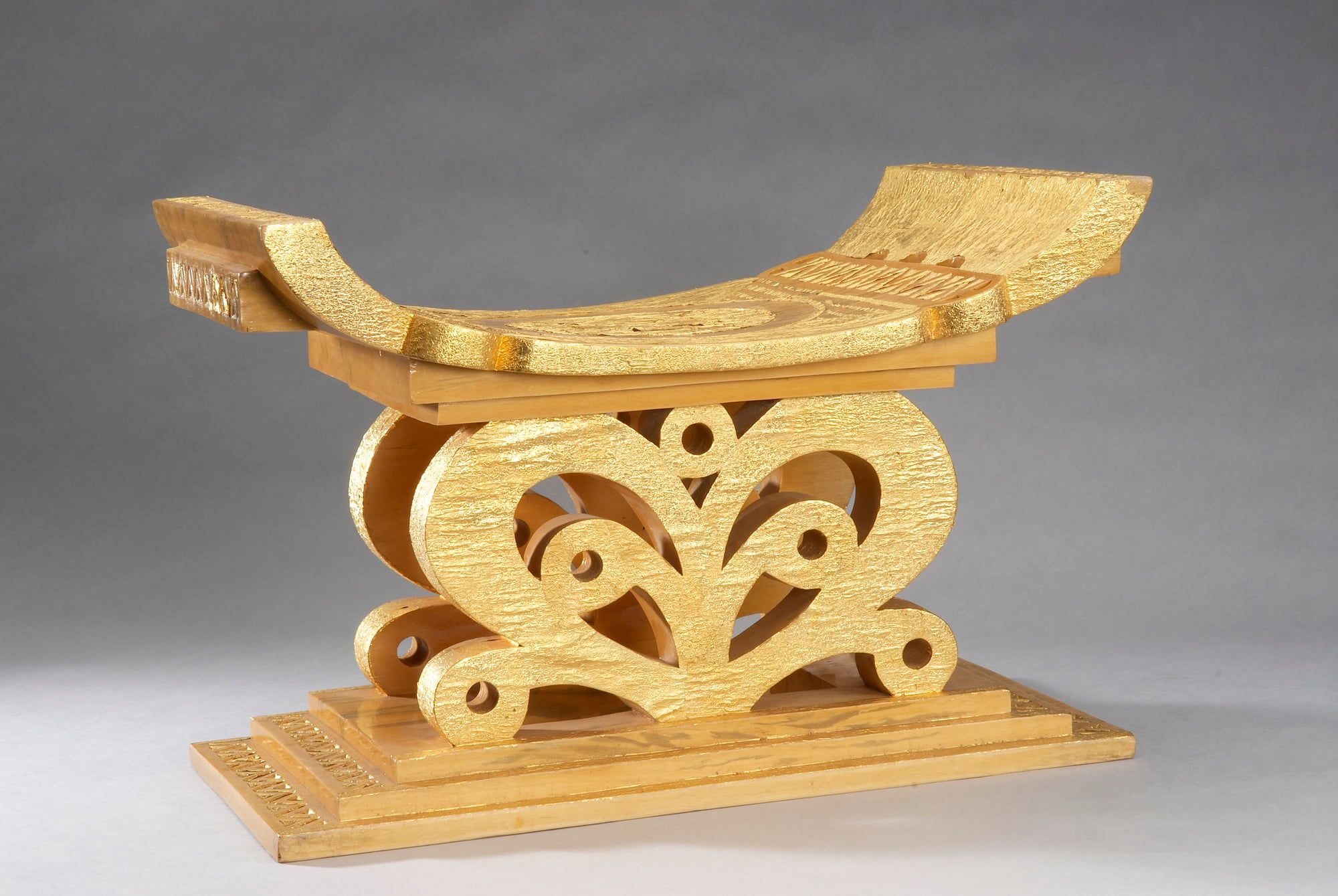 Stool A wooden carved stool with an upturned seat decorated with gold leaf and carved with pierced scrolls.
Ceremonial stools of this kind were made by the Asante people for important chiefs and officeholders. They derive from the foremost symbol of the Asante