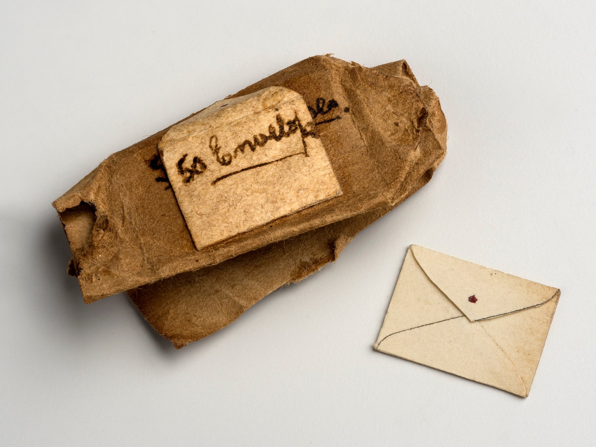 Miniature brown paper package containing envelopes with red crown on flap. Package has been opened. Some envelopes are loose.
