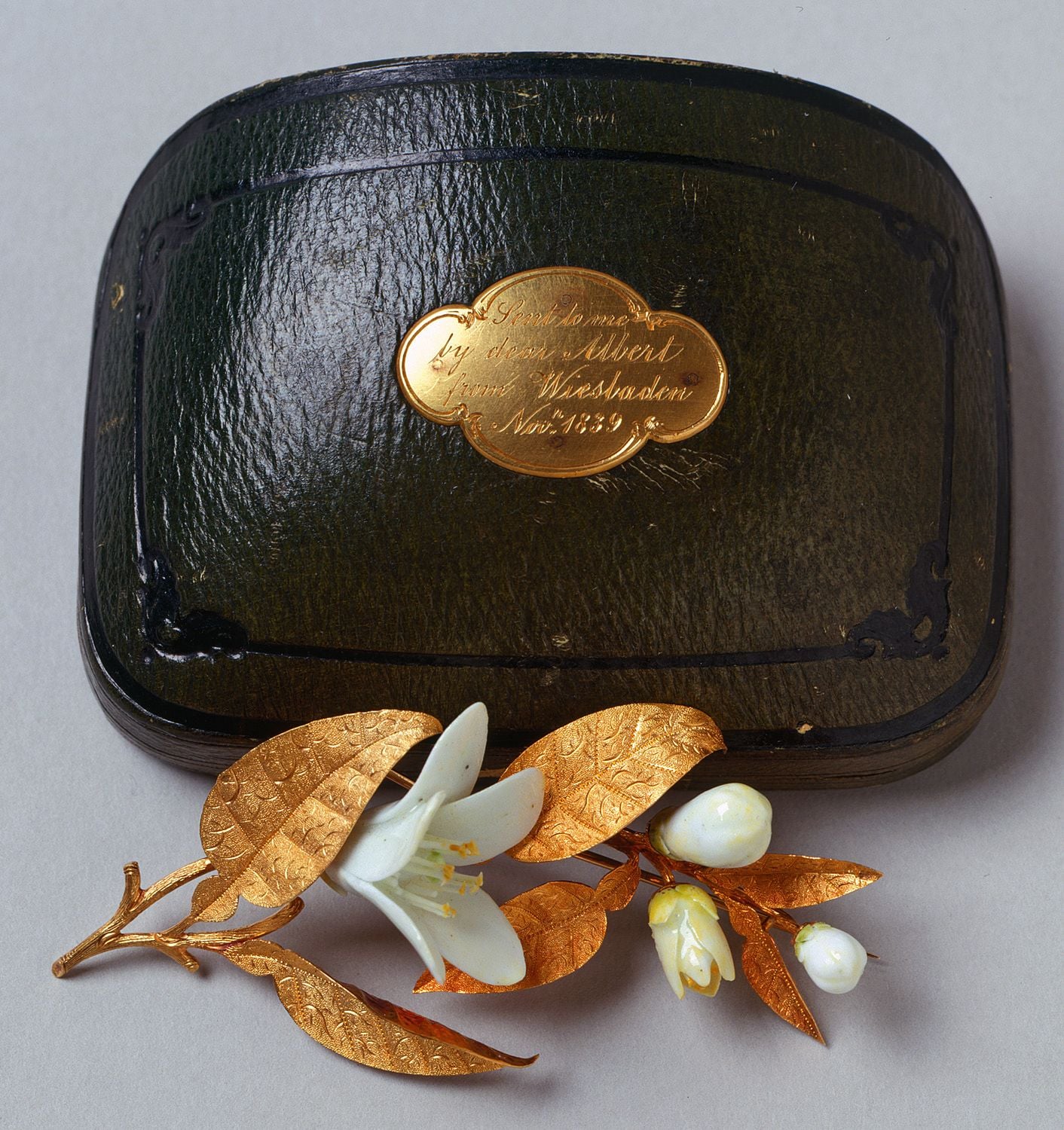 Pair of brooches in the form of a sprig of orange blossom with gold leaves and white porcelain flowers; one in a green leather box mounted with plaque, engraved with inscription: Sent to me/ by dear Albert/ from Wiesbaden/ Novr. 1839.  
 Within the langua