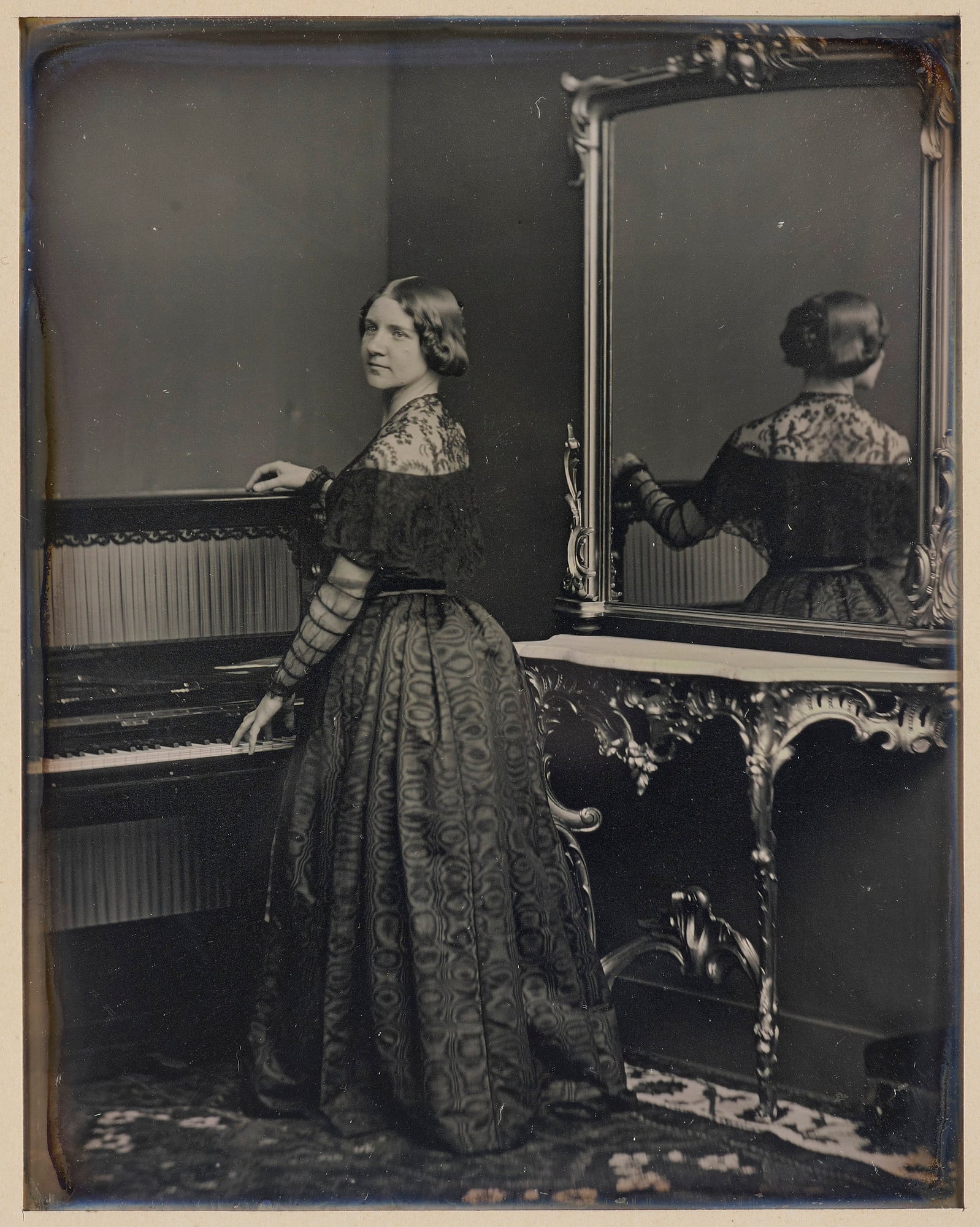 Jenny Lind (1820-1887) Daguerreotype of a full length portrait of Jenny Lind standing beside a piano, facing away from the camera, with her head and upper body turned left towards the camera. Her right hand rests on the top of the piano and her left hand is touching the ke