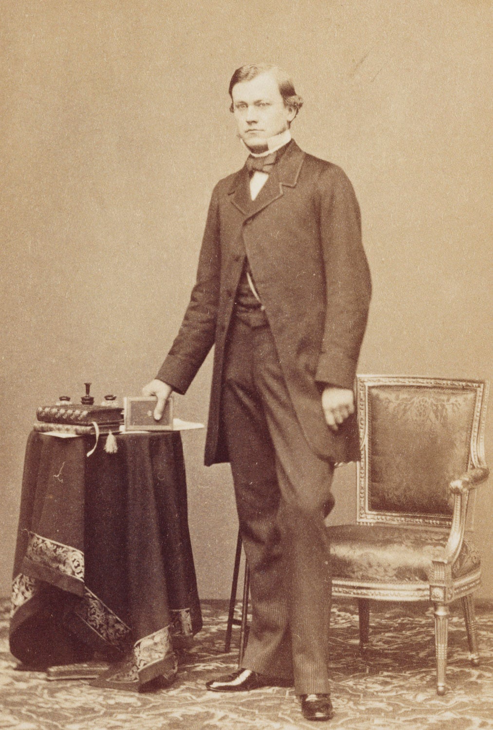Photograph of Carl&nbsp;Ruland, standing beside a chair, holding a book in his right hand, looking at the camera. He was an art and literary historian; Private secretary to Prince Albert and assisted with the Raphael Project.