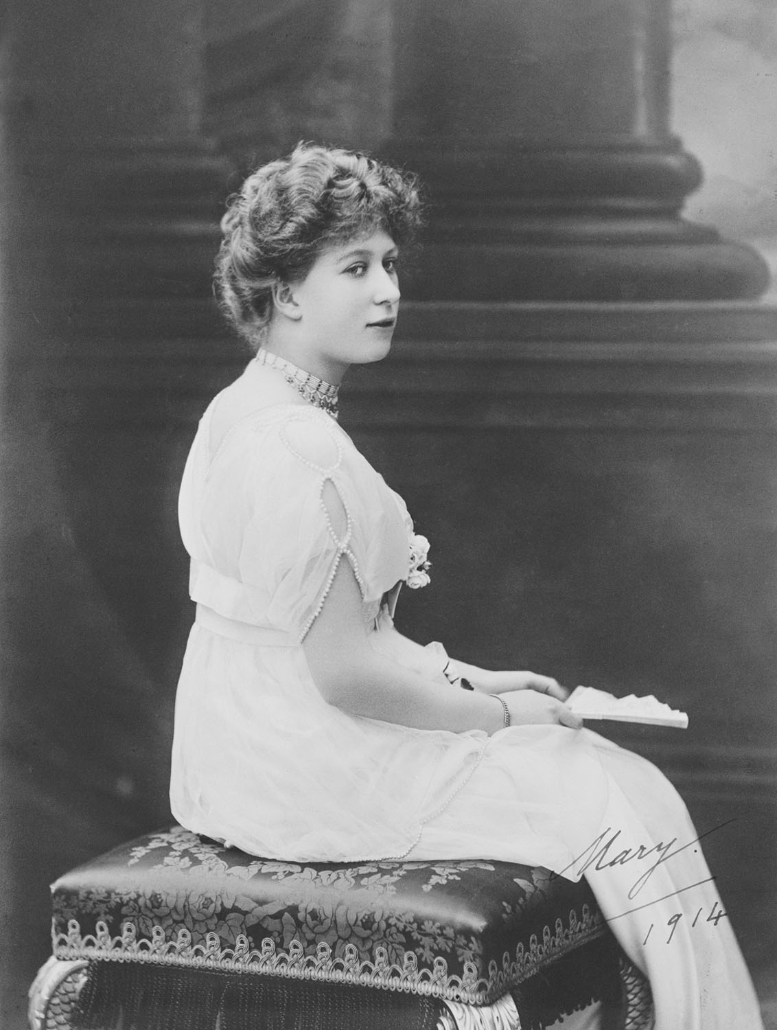 Photograph of Princess Mary (1897-1965), later Princess Royal and&nbsp;Countess of Harewood, in a full length portrait, seated on a stool, with her head turned to face three-quarters to the right. She holds an open fan. Signed by the sitter in the bottom 