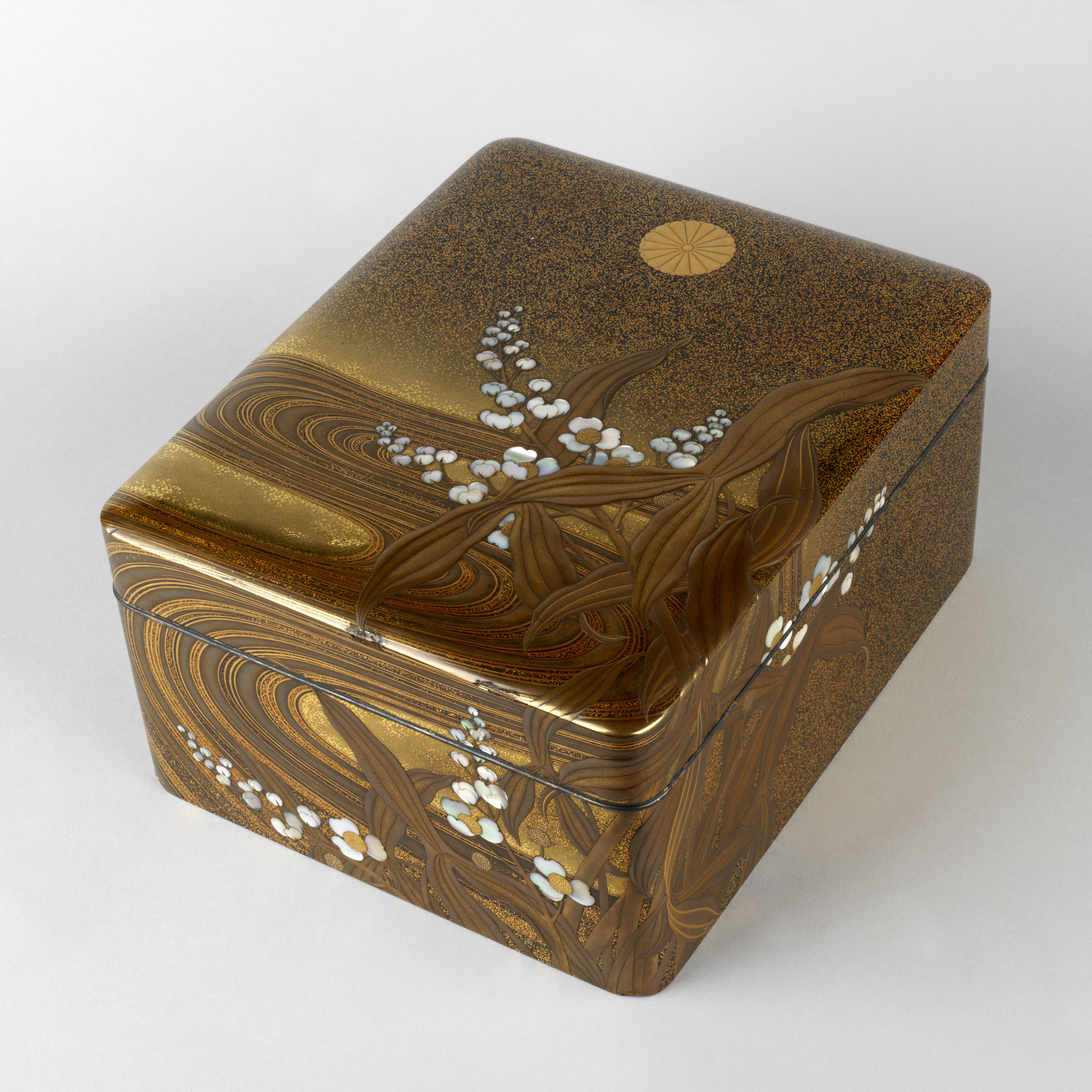 Imperial presentation box and cover Rectangular box, the inset rim fitted with a silver band, the shallow cover similarly fitted, flat-topped and rounded towards the edge.
The large gold chrysanthemum crest (kikumon) on the cover of this box identifies it as an imperial gift. Although unsi