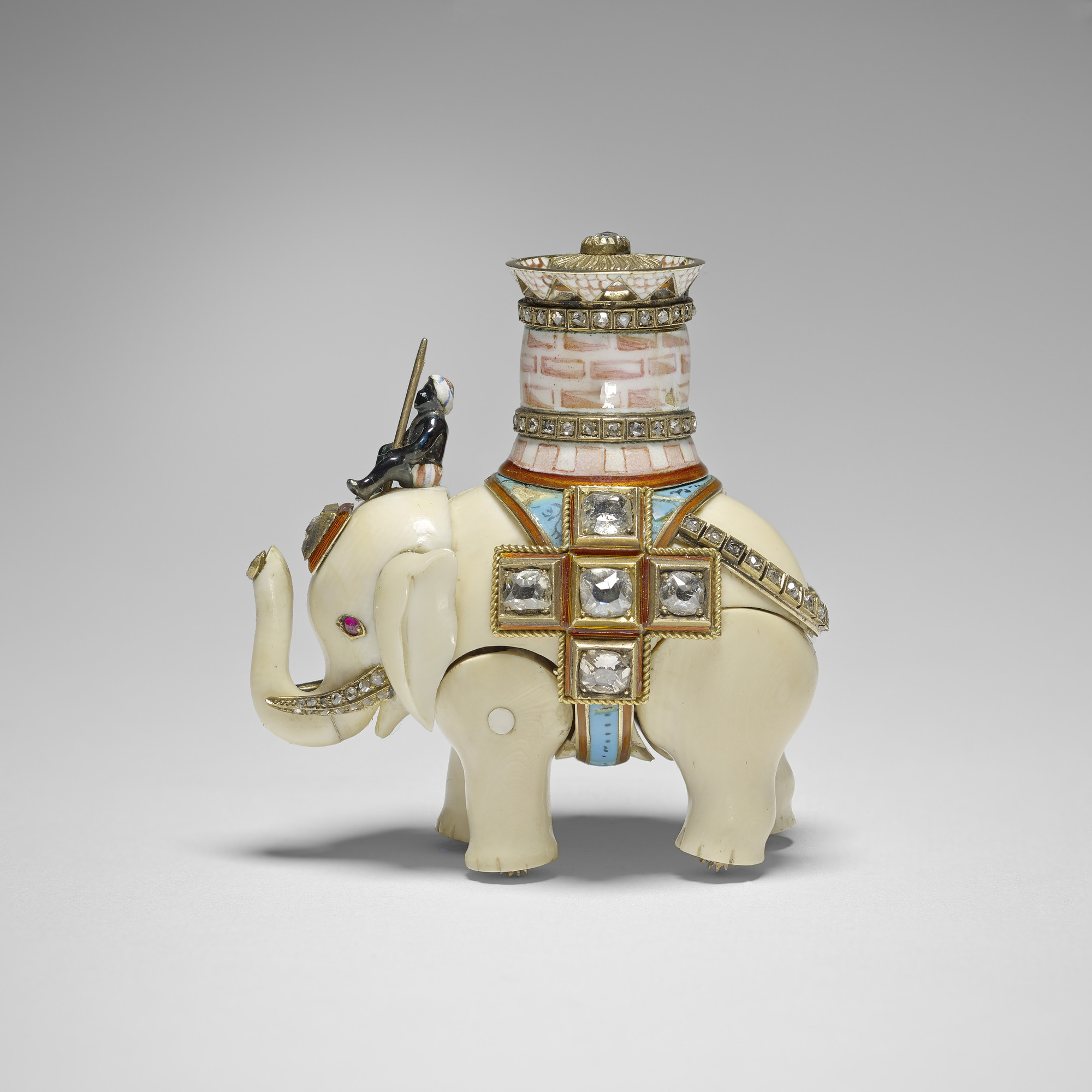 An ivory elephant with separate, jointed body legs&nbsp;and head, ridden by an enamel man sitting on its head&nbsp;and carrying a pink&nbsp;and white enamel castle with two&nbsp; rose cut diamond set bands&nbsp;and a pierced upper rim, the top set with a 