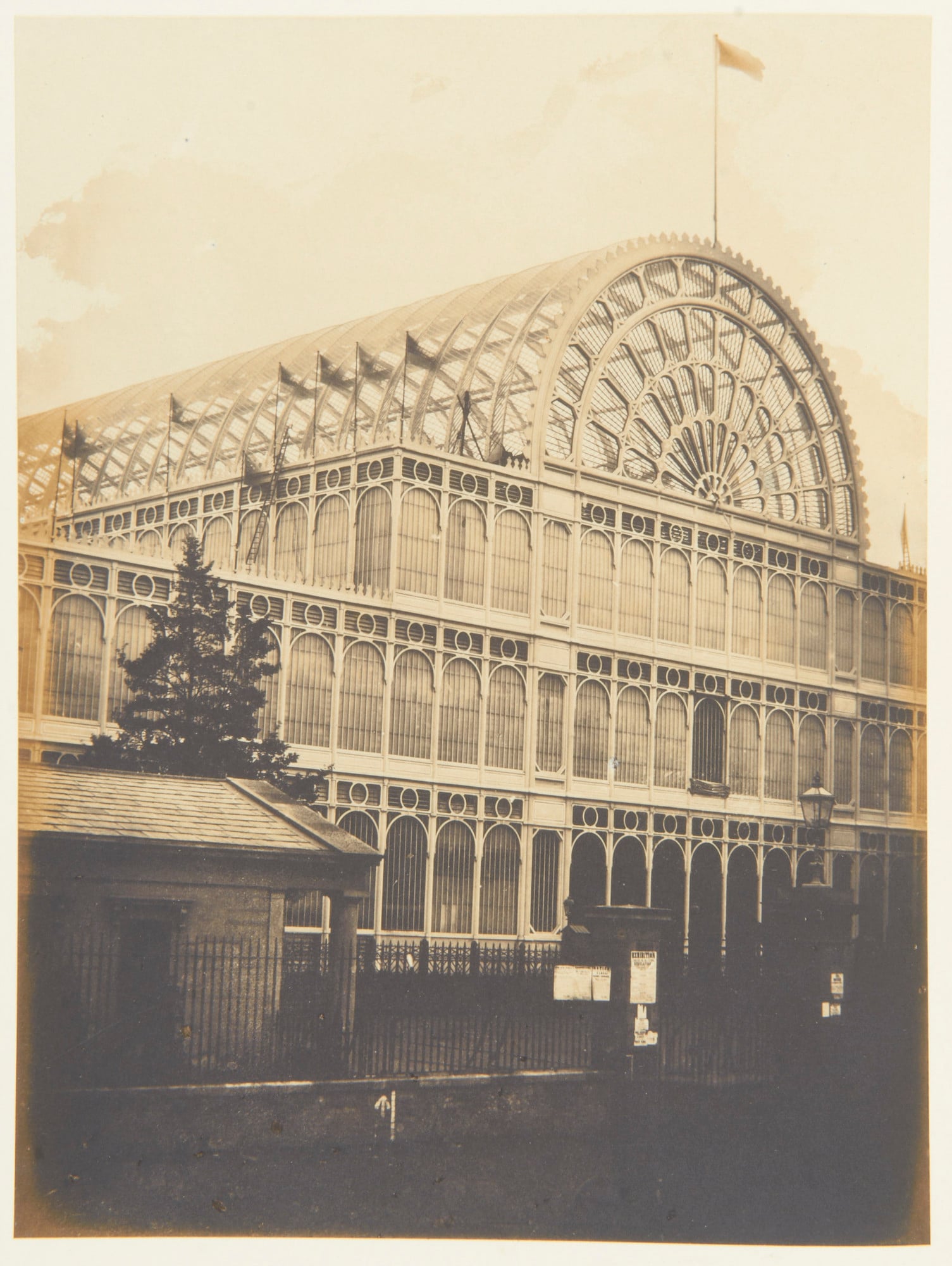 Photograph&nbsp;of an&nbsp;external view of the south transept of the Crystal Palace, Hyde Park during the Great Exhibition.&nbsp;Flags fly along the building and top of&nbsp;the arched roof. 


This photograph is from Volume II (RCIN 2800001) of ' Exhibi