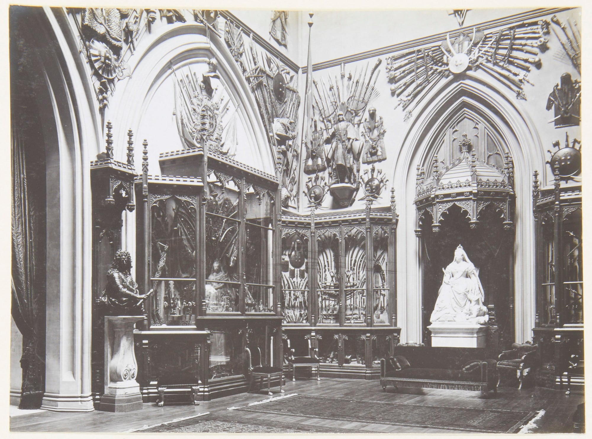 The Grand Vestibule, 1902 Photograph of the Grand Vestibule, with Boehm's statue of Queen Victoria with a collie (RCIN 35336) under a wooden Gothic canopy. The walls are lined with Gothic display cabinets filled with mostly weapons; above them are displays of a