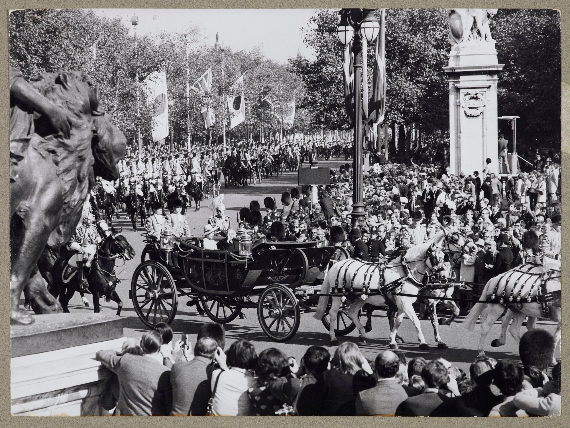 Photograph of a general view looking down the Mall from the Queen Victoria Memorial statue with St James' Park on the right&nbsp;where thousands of people wave to Emperor Hirohito who rides alongside HM the Queen in a carriage during&nbsp;the State Drive 