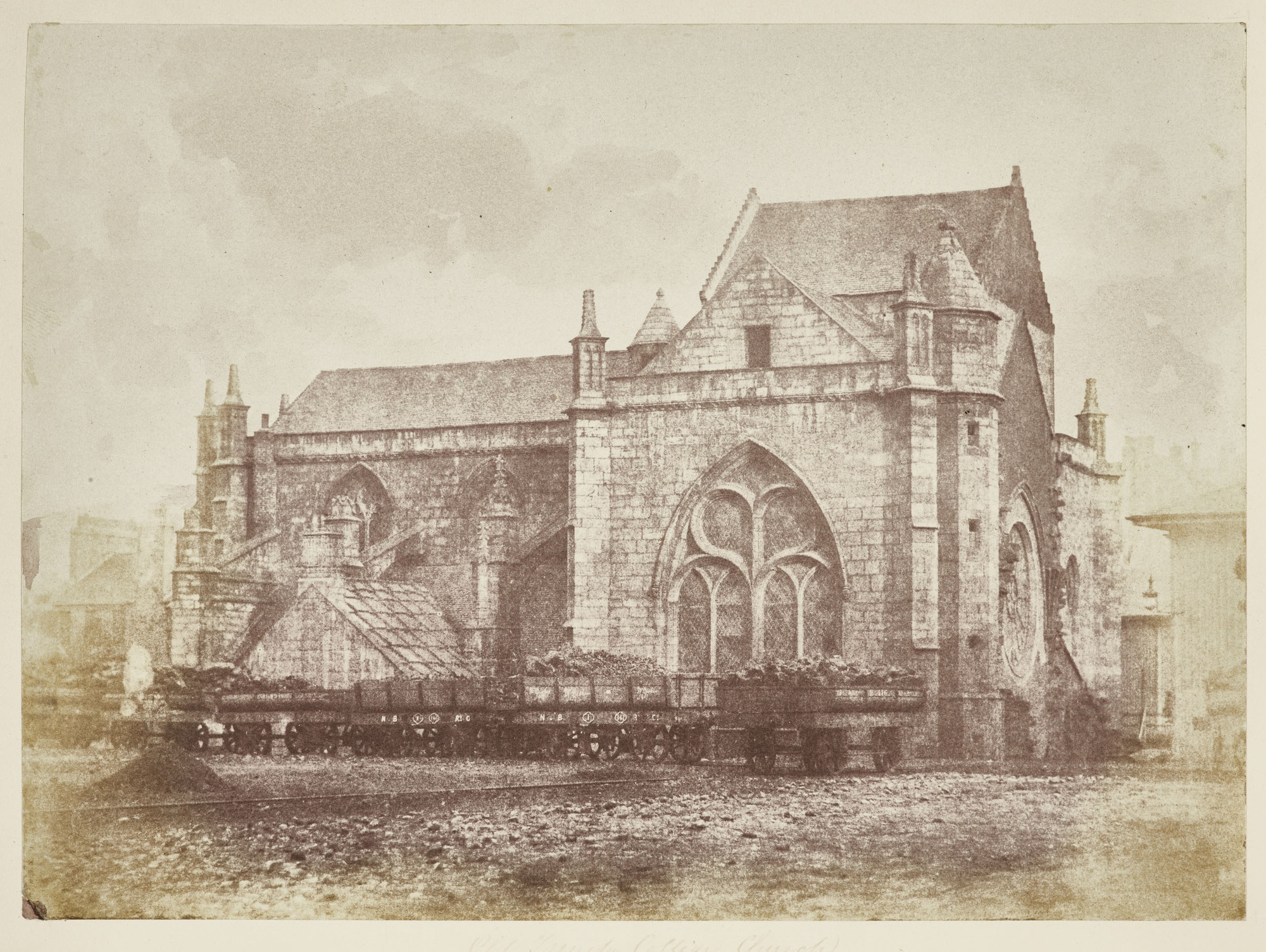 Old Trinity College Church, Edinburgh Photograph of Trinity College Church with railway goods wagons in the foreground. On the main wall facing the viewer is a large gothic arch stained glass window and on the right side is a large rose window. Flying buttresses on the left with a smaller bui