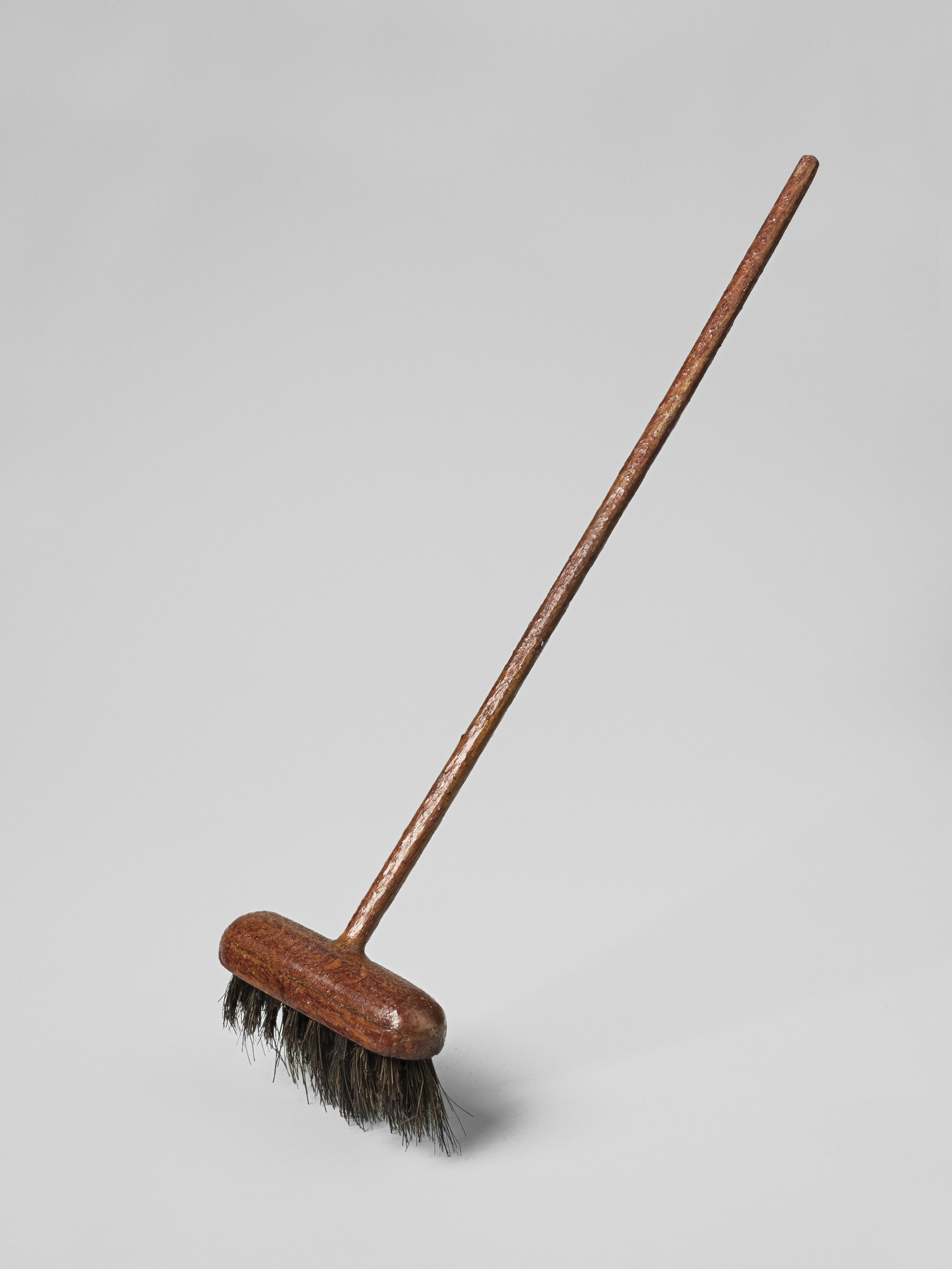 Miniature red painted wooden broom with dark bristles