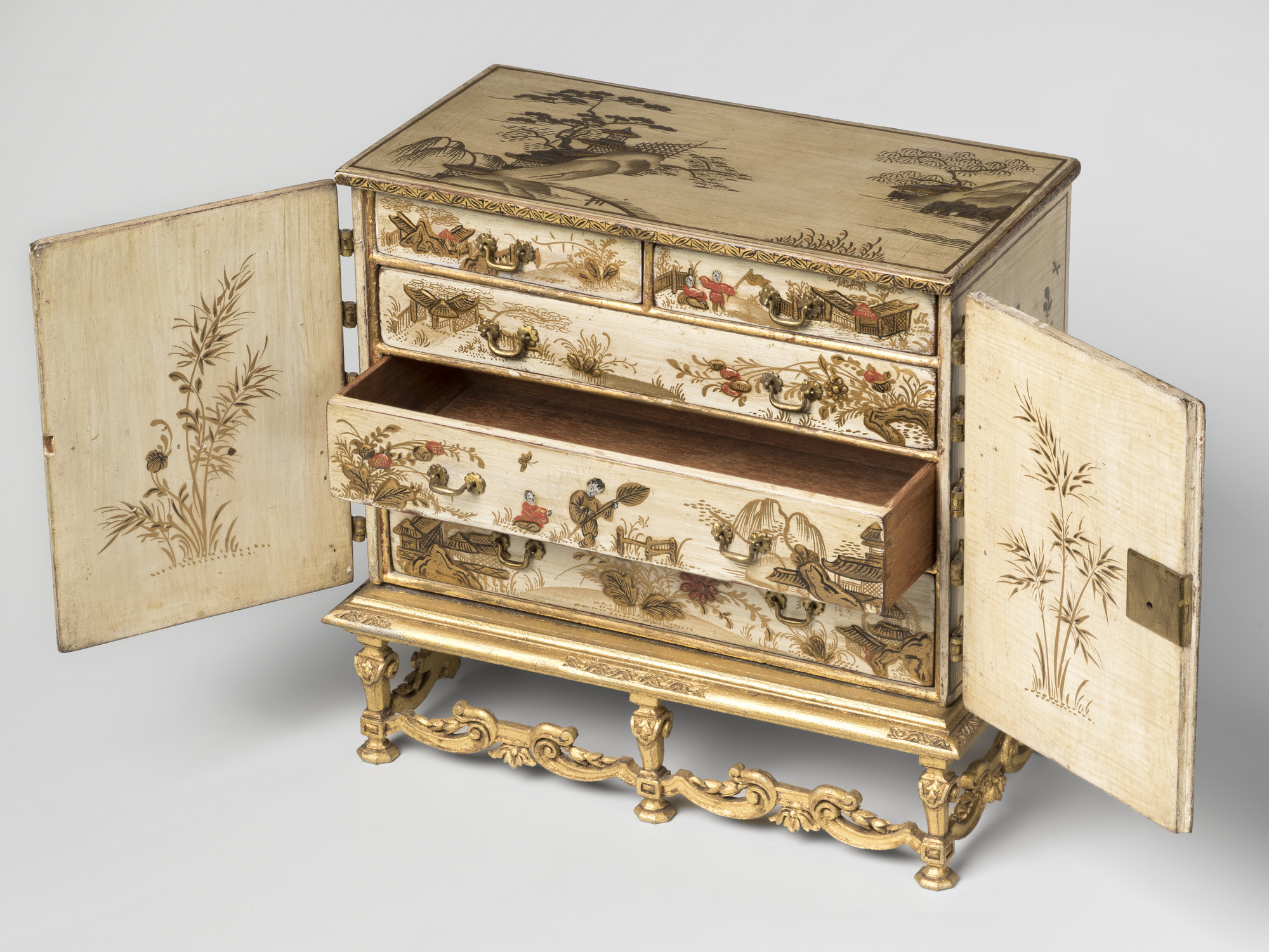 Miniature lacquered cabinet on stand. Cream ground, lacquered with oriental scenes, temple and figures in gold&nbsp;and red; top with mountain&nbsp;and buildings.&nbsp;Two front opening doors with brass hinges. Interior with two short over&nbsp;three long