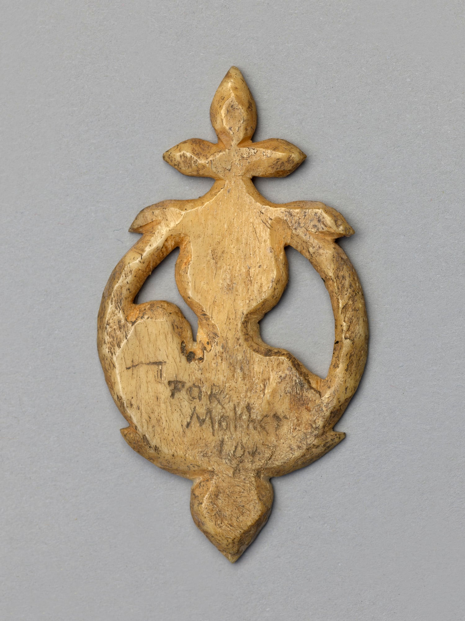 <p>Token</p> To pass the time in the trenches, many soldiers made carvings out of the materials they had to hand. This token depicting the Madonna and Child is made from the bone of an ass and was carved using a pocket knife and a packing needle. It was made by Piper