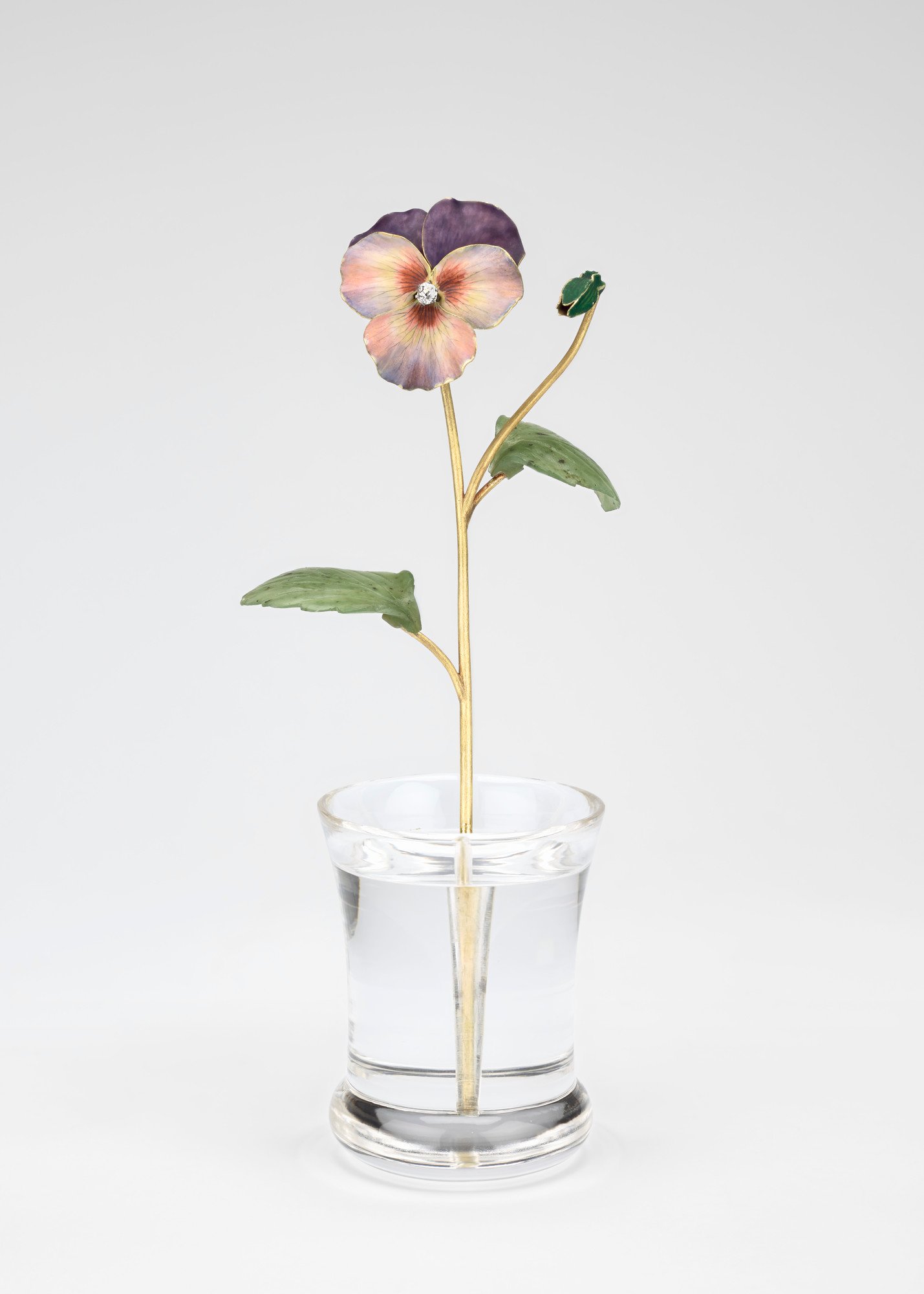 A single pansy with bud, enamelled with opaque violet and with a brilliant diamond centre, two nephrite leaves are attached to the green gold stalk, all set in a rock crystal pot. 
The pansy was almost as popular as the philadelphus in Russia, flowering i