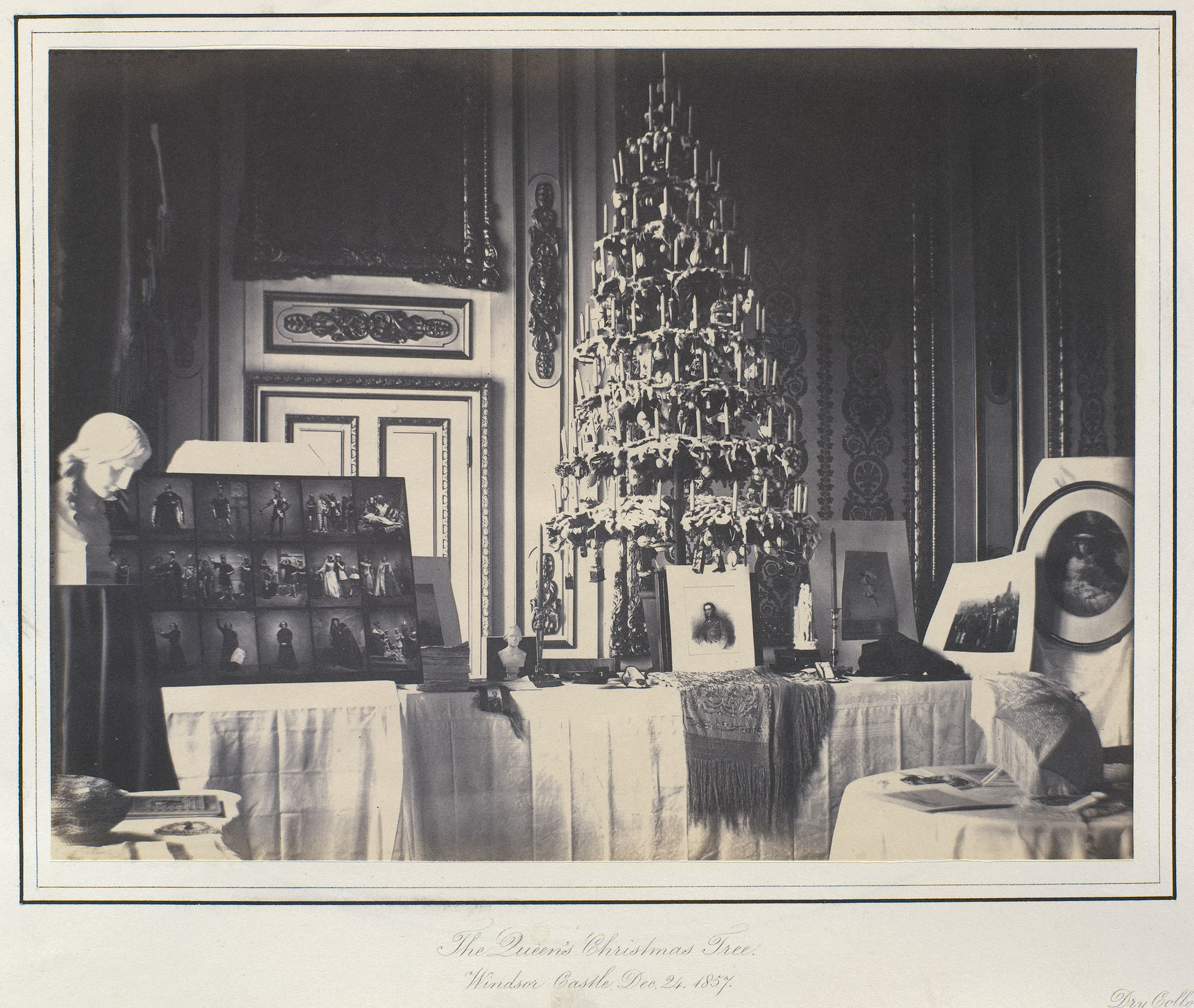Photograph showing a decorated Christmas tree on top of a table surrounded by various gifts that include photographs and ornaments.
Queen Victoria and Prince Albert did much to popularise the German custom of decorating fir trees at Christmas time, which 