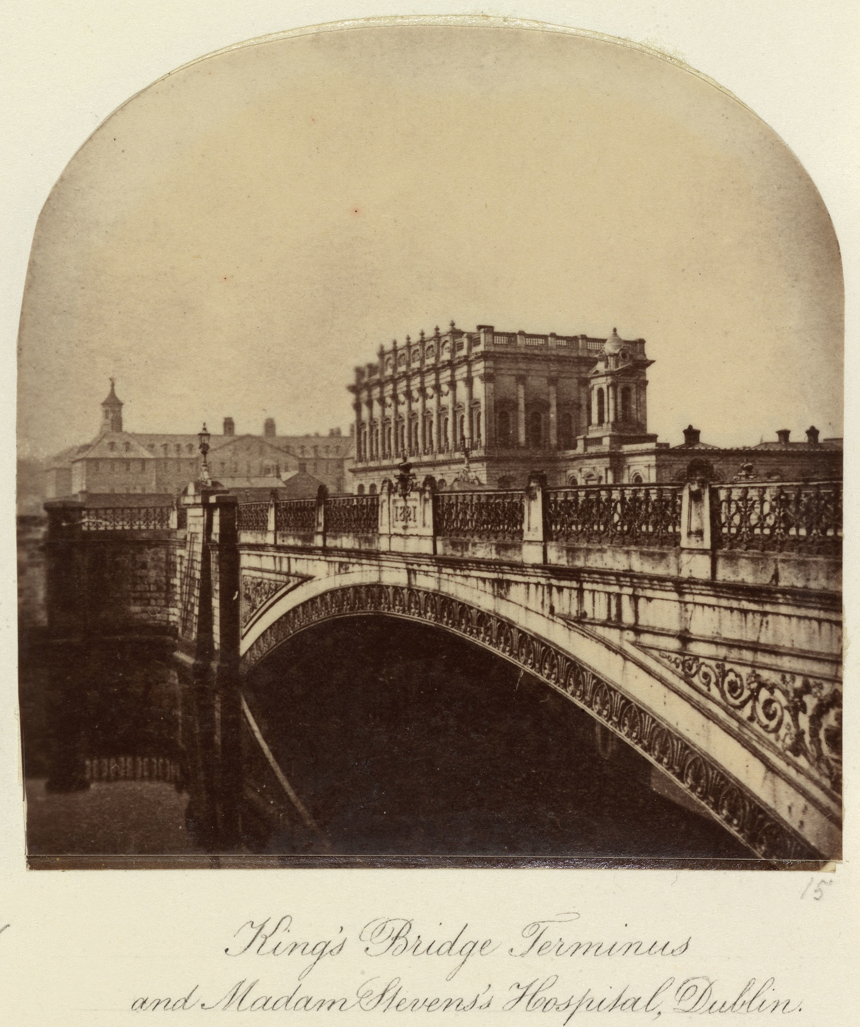 Photograph of a view of Kingsbridge Station, now Hueston Station, Dublin. Kings Bridge, now Se&aacute;n Hueston Bridge, and the River Liffey are located in the foreground. The bridge is reflected on the water's surface. Dr Steeven's Hospital, commonly kno