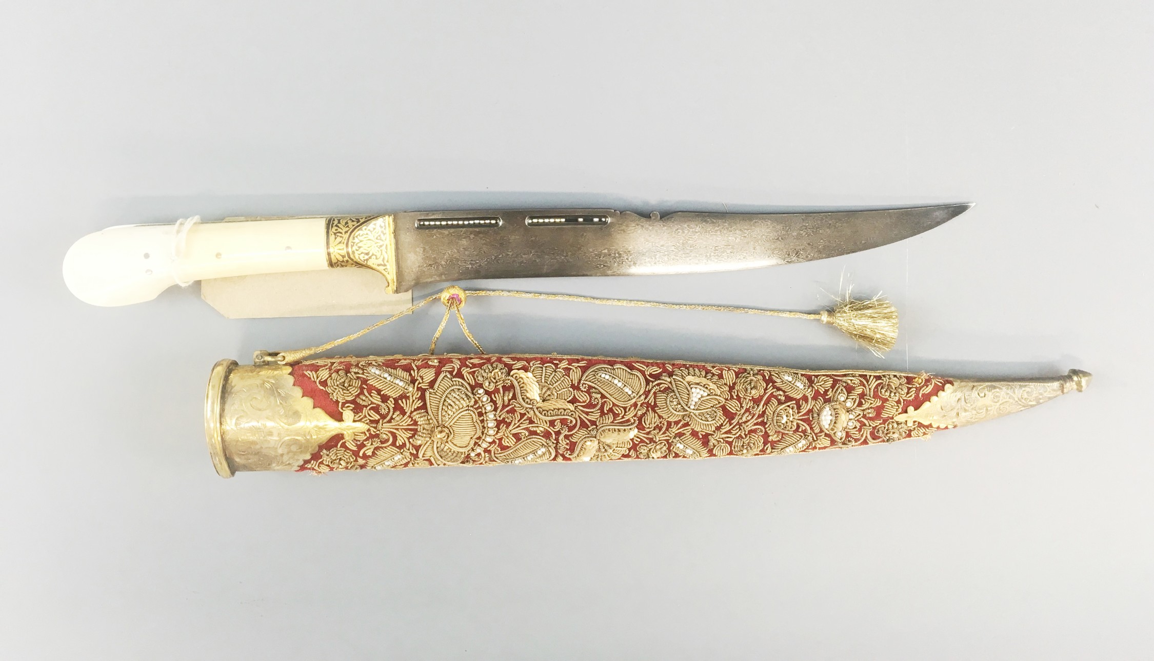 Dagger and sheath An Indian dagger: the ivory handle with bifurcated pommel divided by gilt-metal side-plates; the steel ferrule with gilt flowers and foliage. Watered steel back-edged blade with two narrow rectanglular cut-outs set with seed pearls. Red velvet