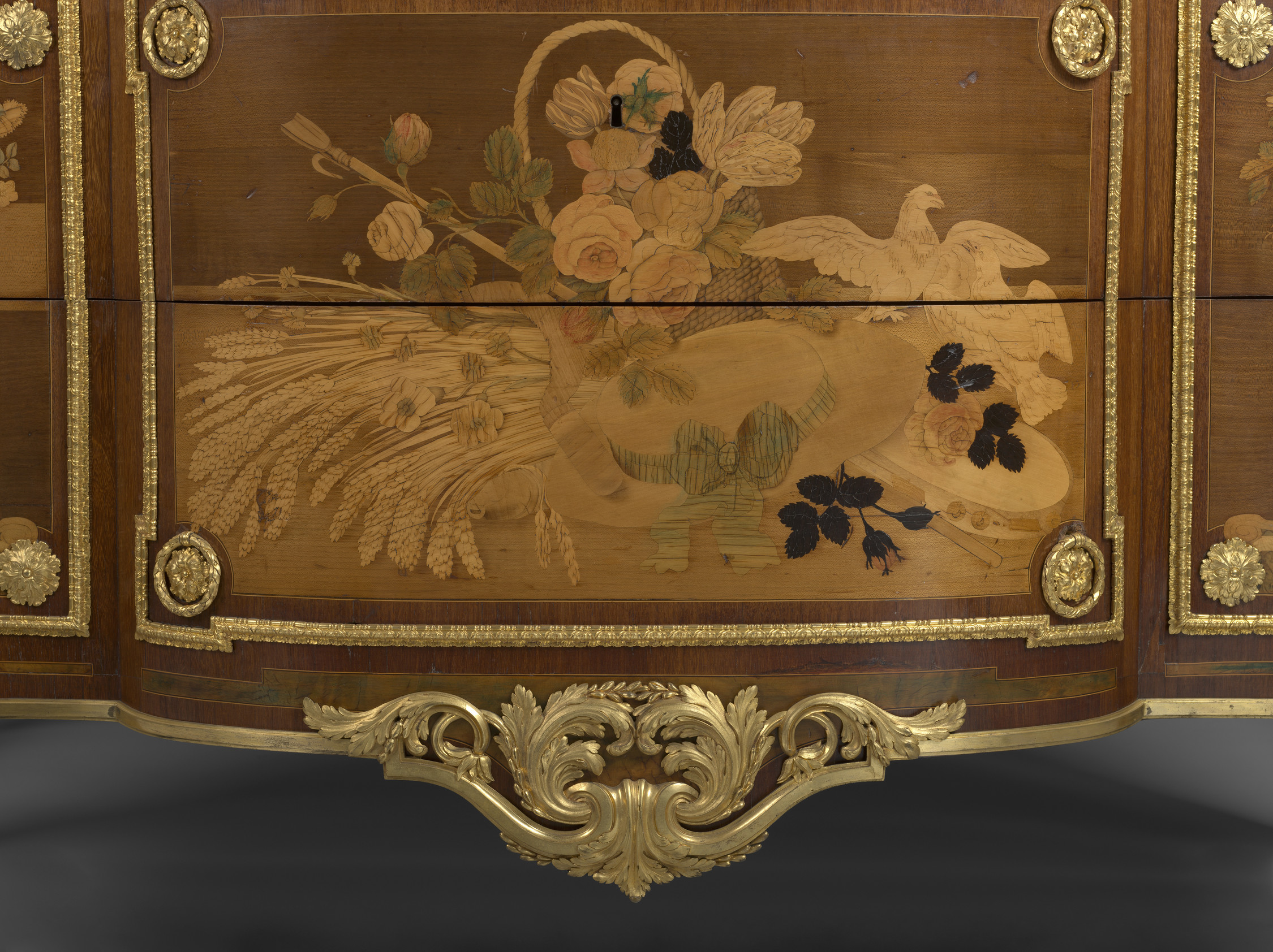 Rectangular commode with curved front, angled corners and red griotte marble top. Two large drawers with large central gilt bronze frame enclosing marquetry panels of a basket of flowers, sheaves of corn, a hat, a shepherd's hoe and two birds; flanked by 