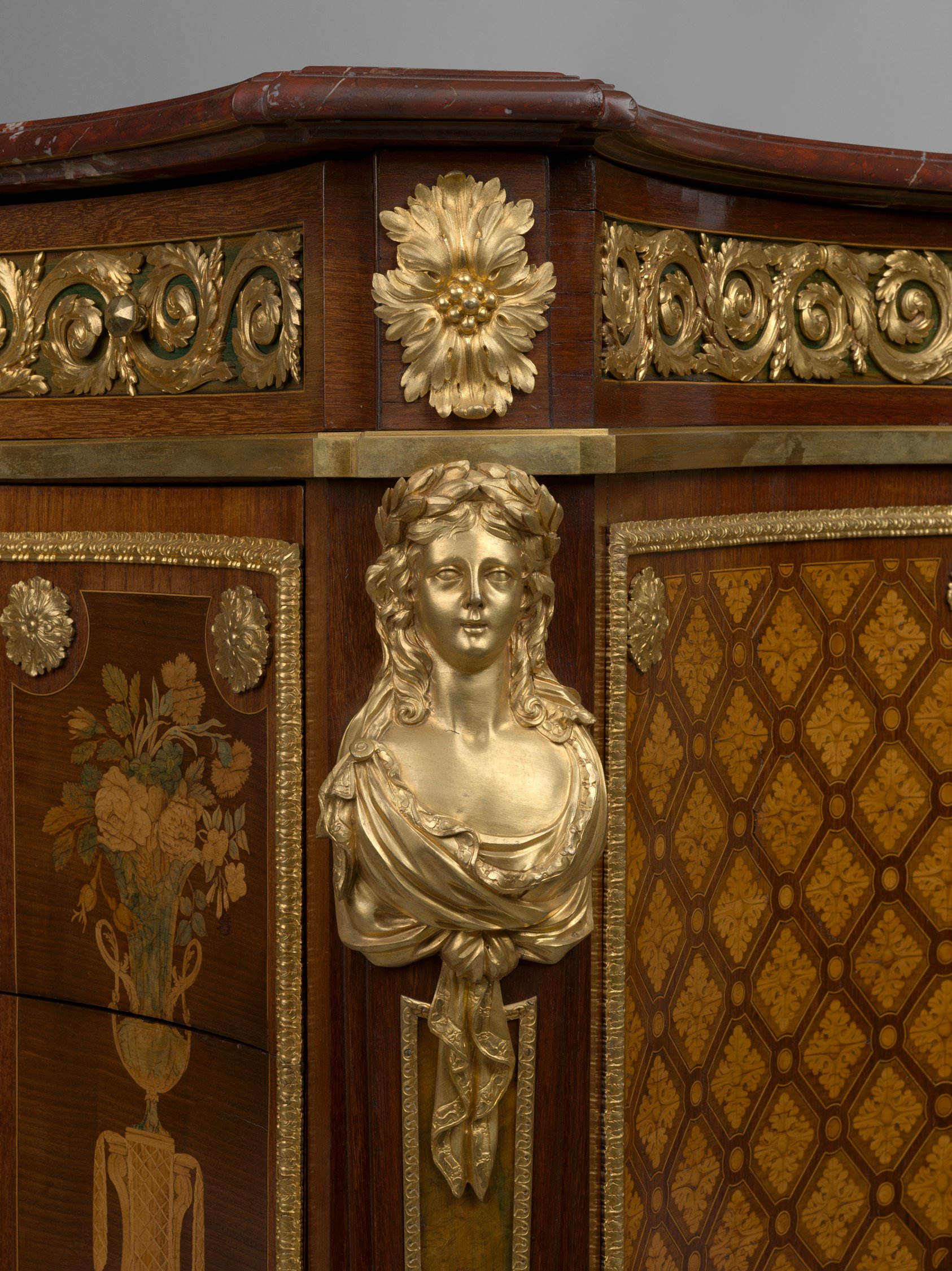 Rectangular commode with curved front, angled corners and red griotte marble top. Two large drawers with large central gilt bronze frame enclosing marquetry panels of a basket of flowers, sheaves of corn, a hat, a shepherd's hoe and two birds; flanked by 