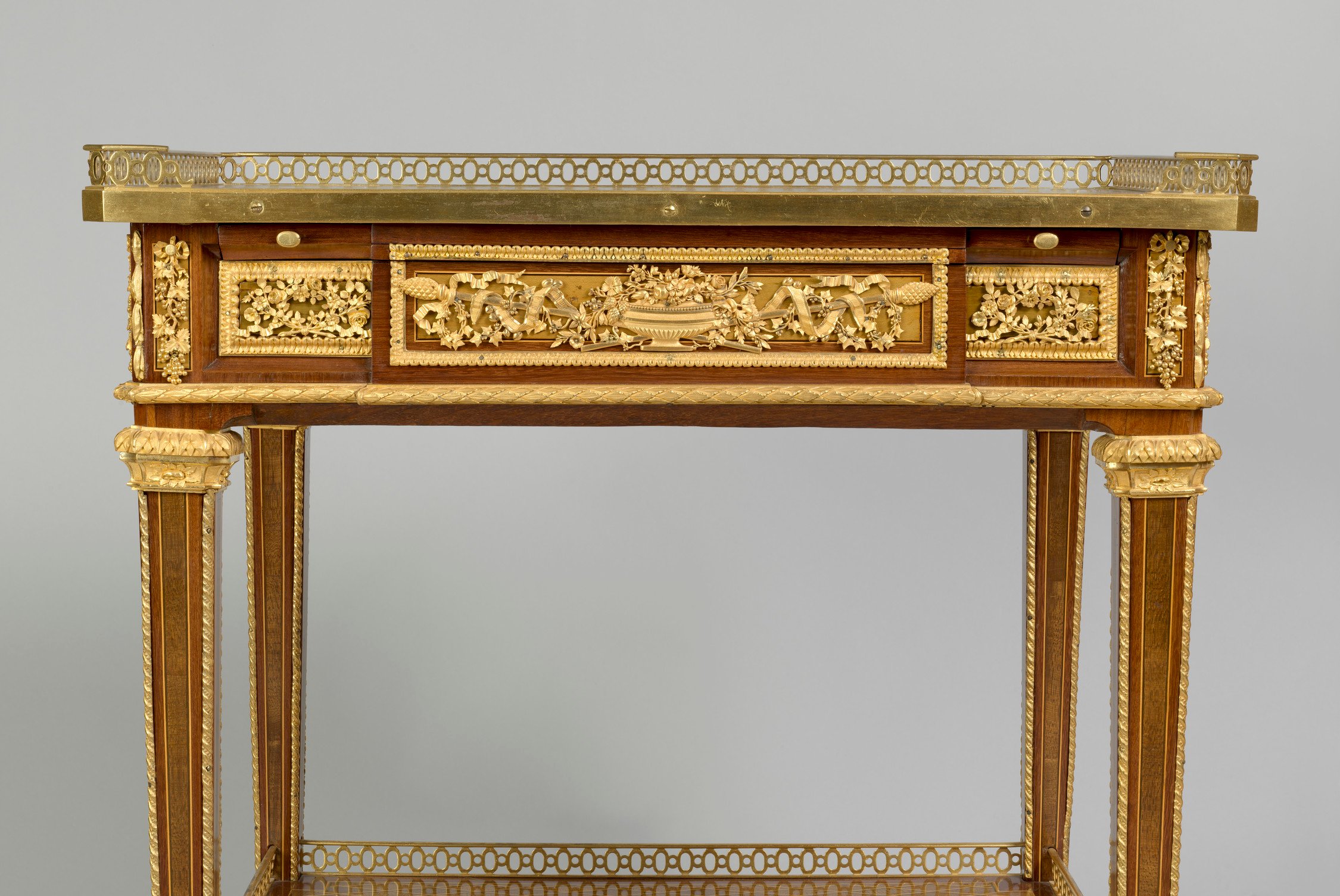 The rectangular trellis parquetry top with pierced three-quarter gilt bronze gallery above a&nbsp;panelled frieze with&nbsp;a drawer&nbsp;on one long side incorporating a&nbsp;ratcheted&nbsp;leather-lined writing-slide, and a small pen drawer on the right