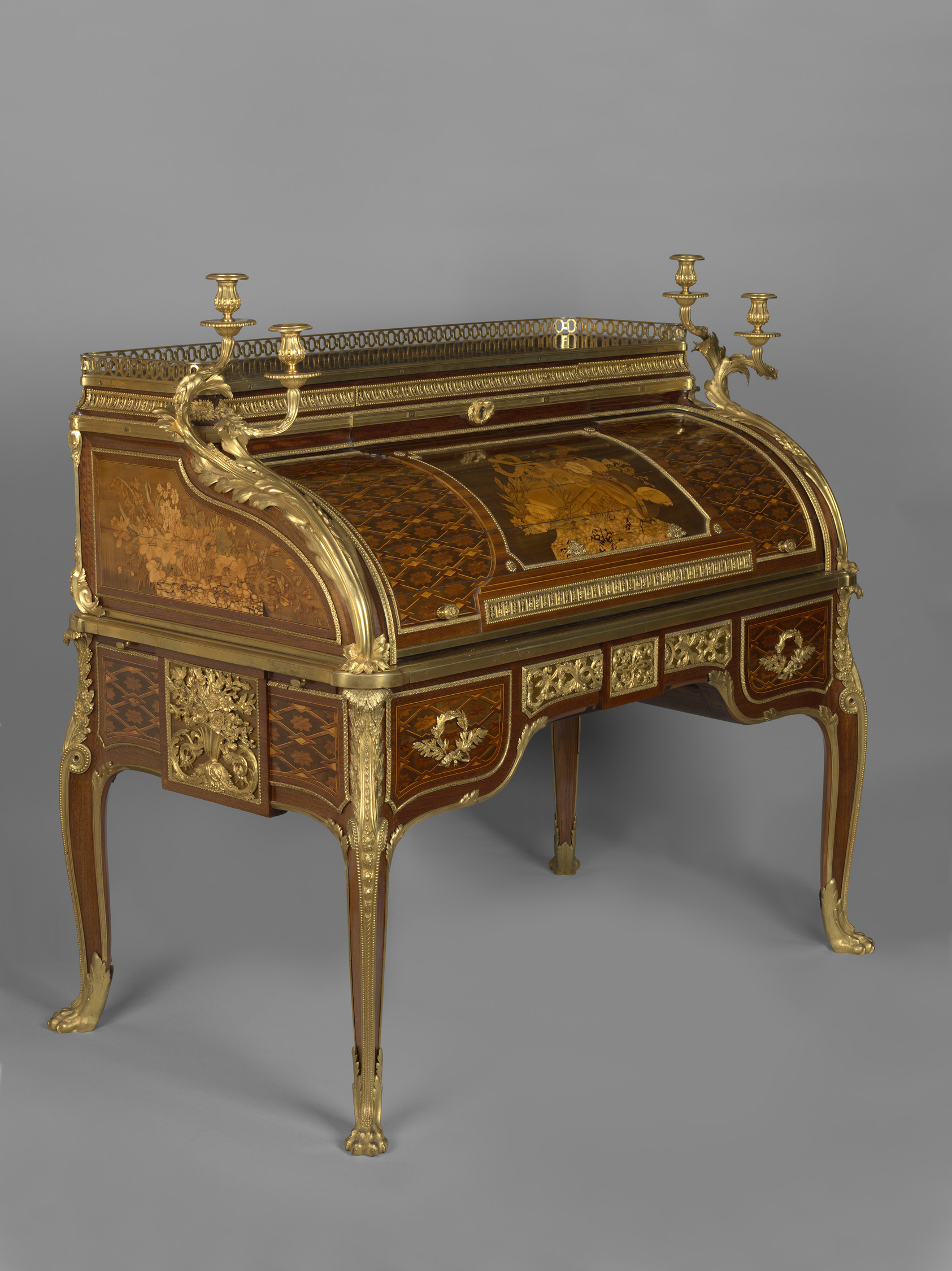 Roll-top desk veneered in purplewood, mahogany, casuarina wood, holly, boxwood, sycamore and other woods, partly stained and engraved. The top,&nbsp;surrounded by a pierced gilt bronze gallery, is fitted with three drawers, the central&nbsp;drawer forming