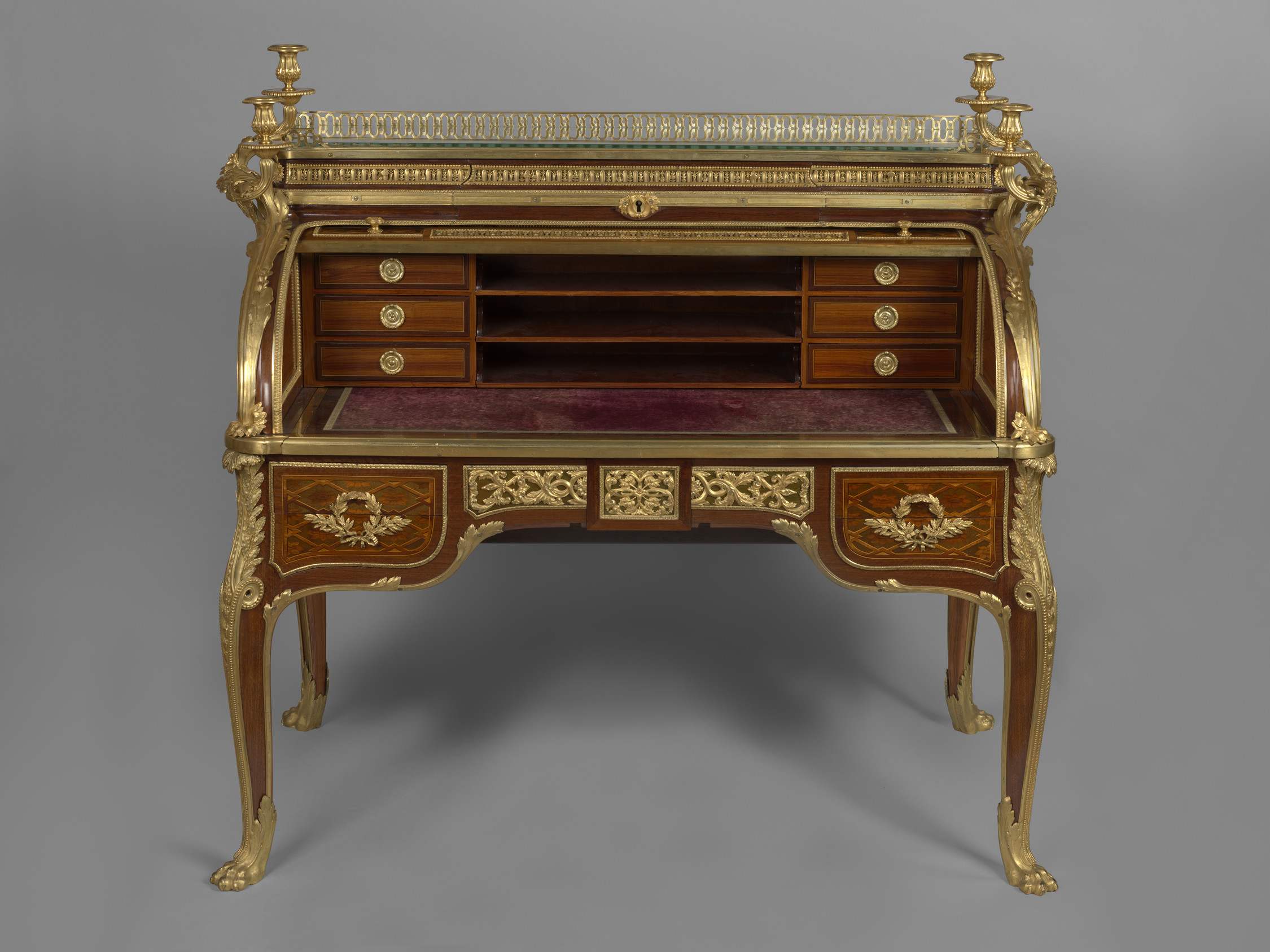 Roll-top desk veneered in purplewood, mahogany, casuarina wood, holly, boxwood, sycamore and other woods, partly stained and engraved. The top,&nbsp;surrounded by a pierced gilt bronze gallery, is fitted with three drawers, the central&nbsp;drawer forming