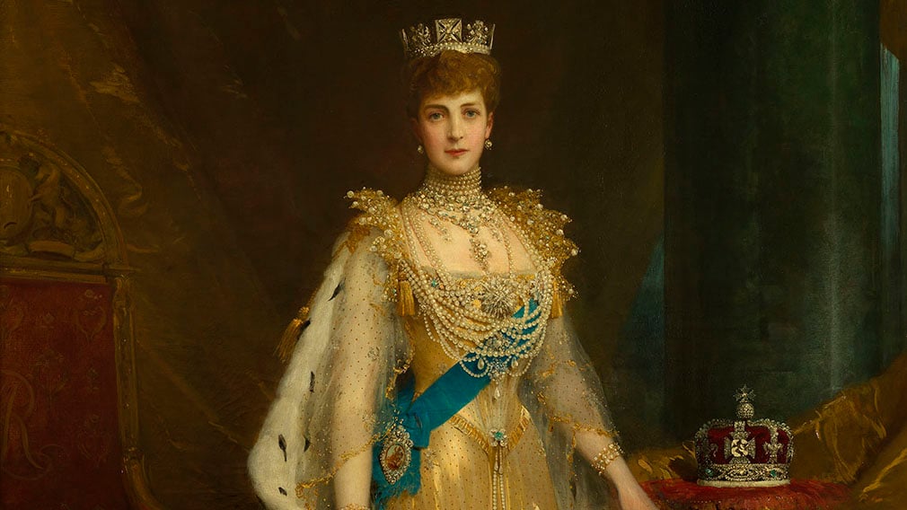 Portrait of Queen Alexandra wearing coronation robes. Her crown rests on a cushion (RCIN 404554) Painting of Queen Alexandra wearing red coronation robes over a gold dress. A crown rests on a cushion to the right.