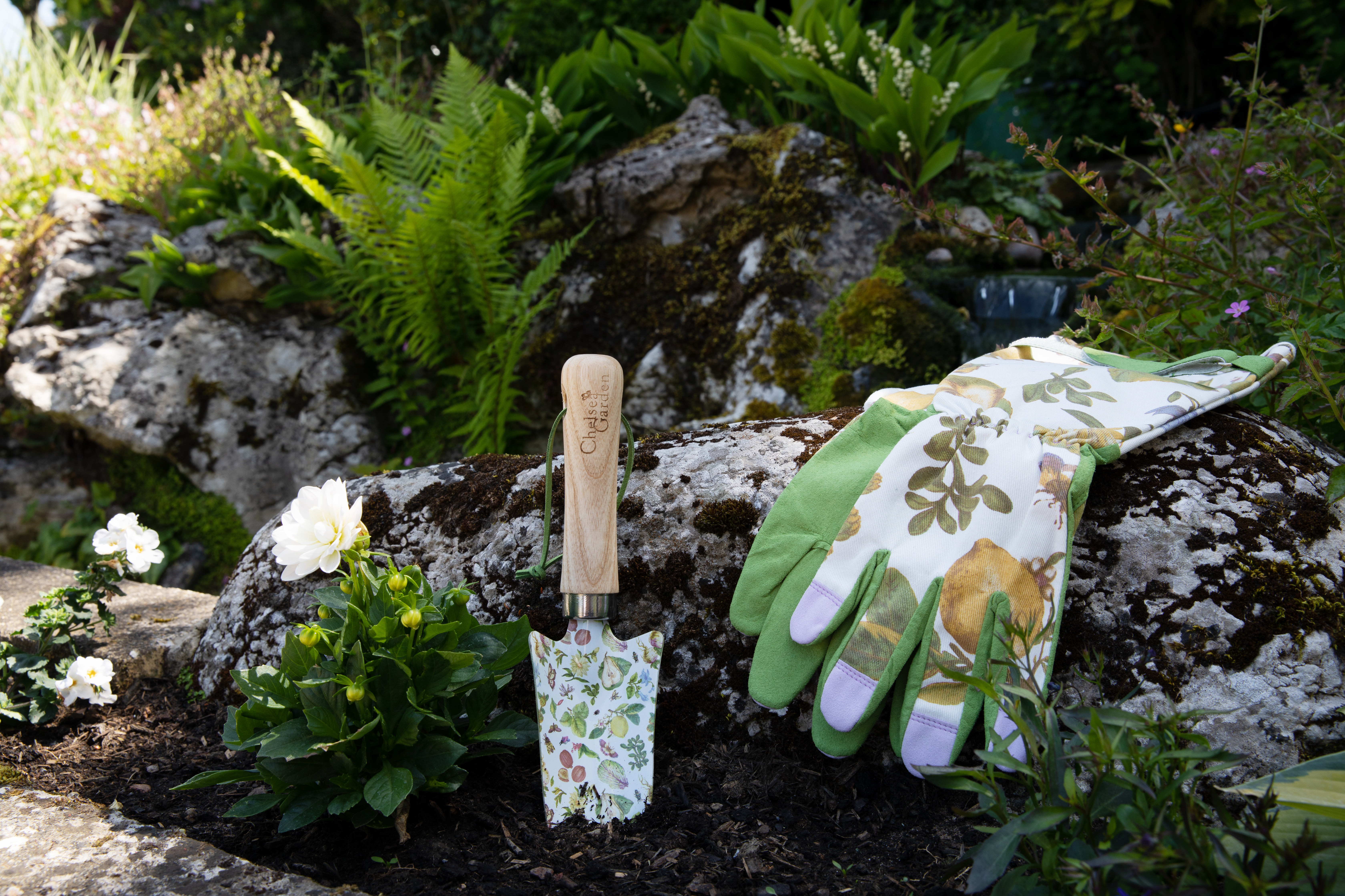 The trowel being used in a garden, with the gardening gloves lying on a rock