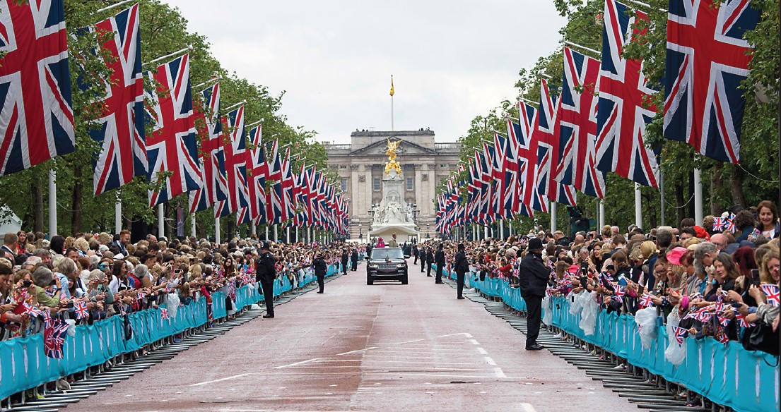 large crowds line the mall which is decorated with flags and Buckingham Palace can be seen in the background