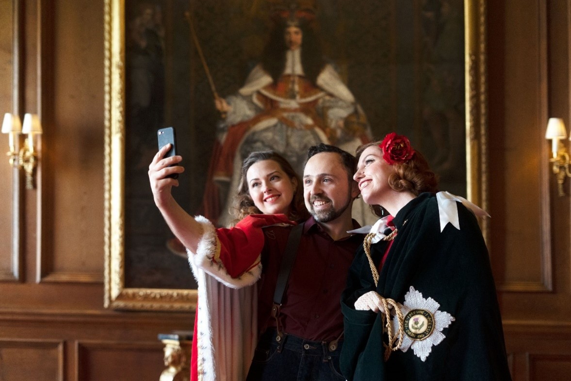 Three people smile while taking a selfie in the Palace of Holyroodhouse