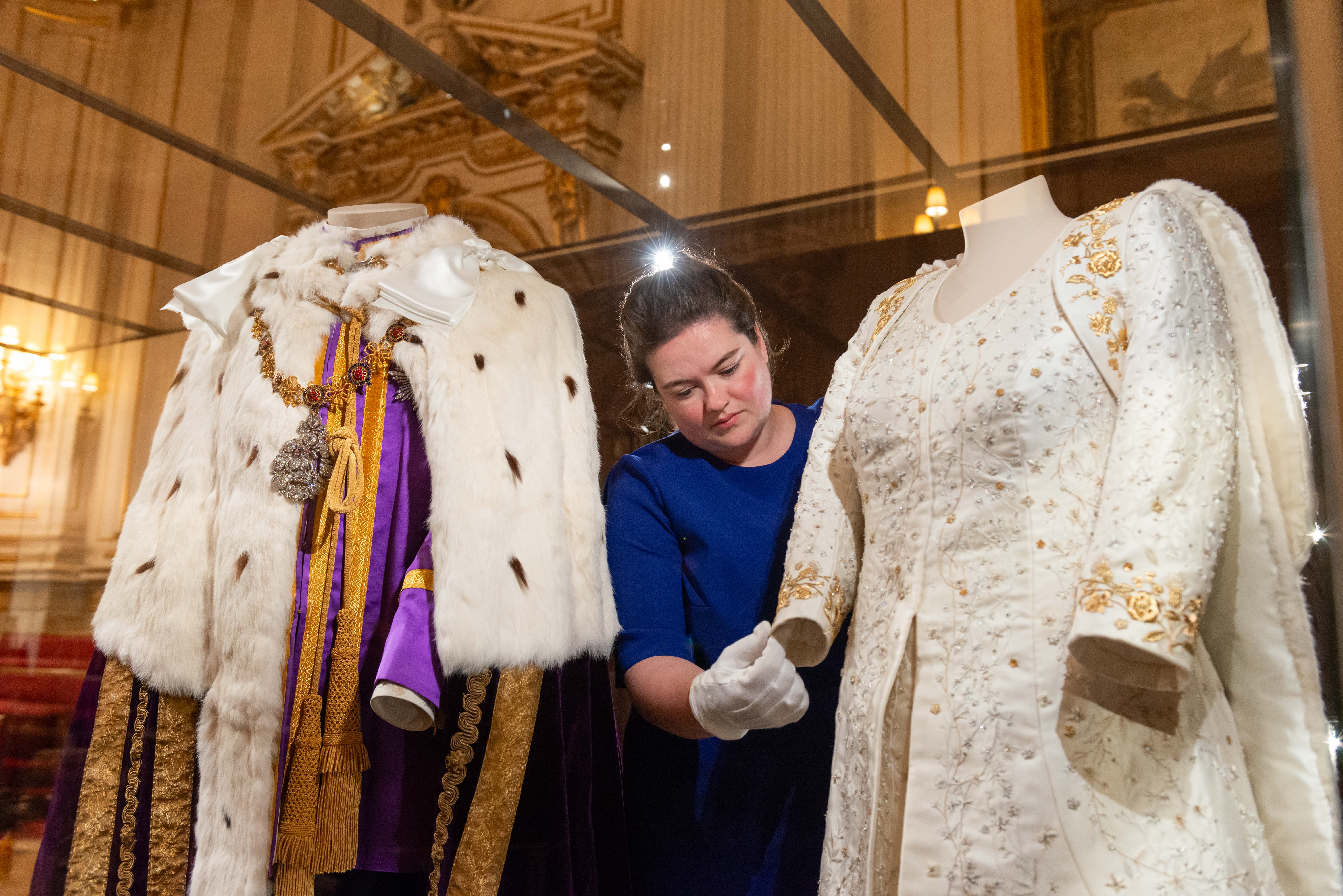 The curator makes final adjustments to The Queen’s Coronation Dress. The curator makes final adjustments to The Queen’s Coronation Dress next to The King’s Robe of Estate