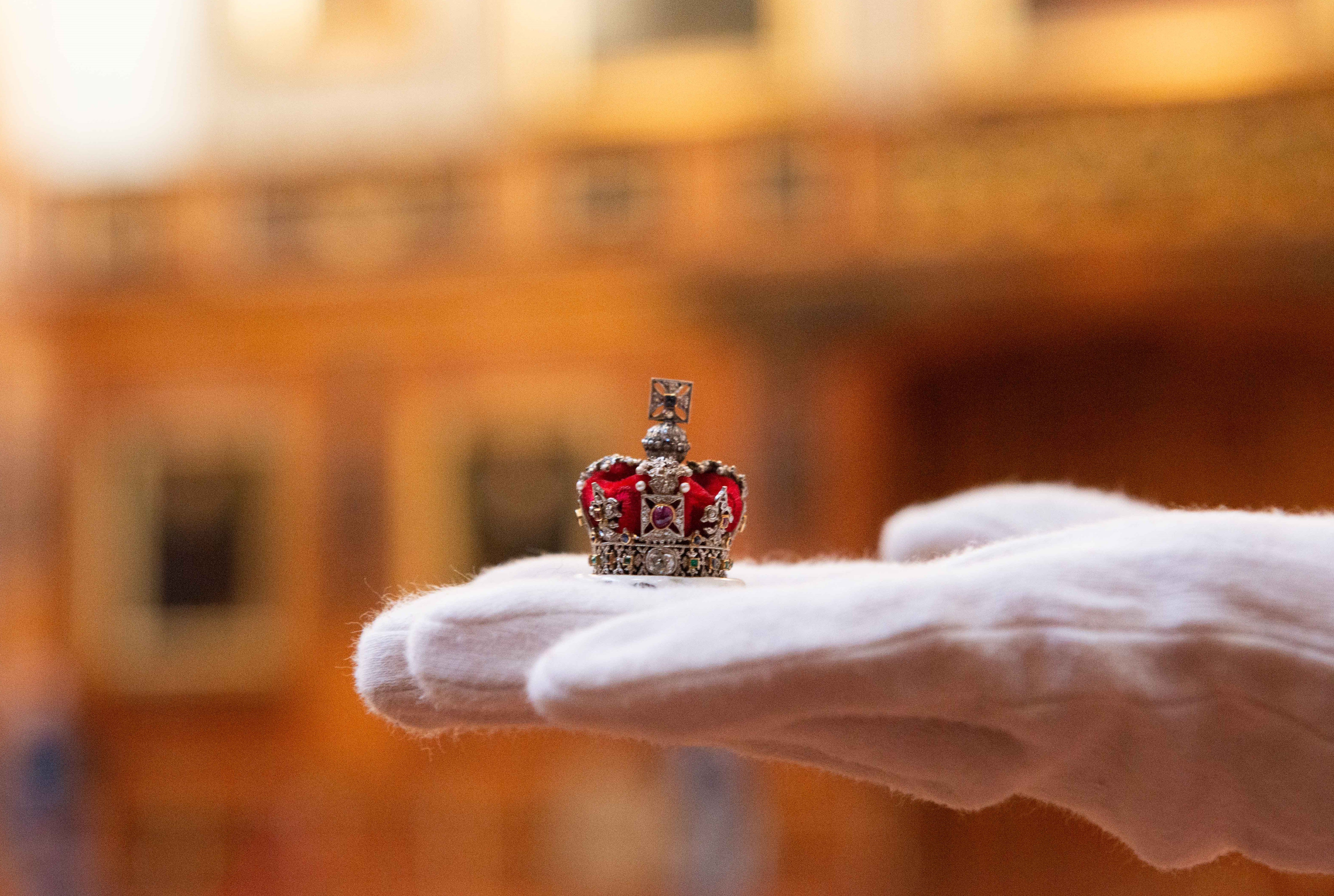 A miniature crown is held by the curator with a white glove 
