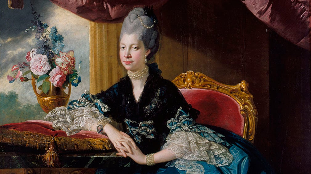 Queen Charlotte (RCIN 405071) Queen Charlotte sitting on a red velvet chair wearing a blue silk dress with white lace. She also wears a black shawl. A vase of flowers sits on a table on her left.