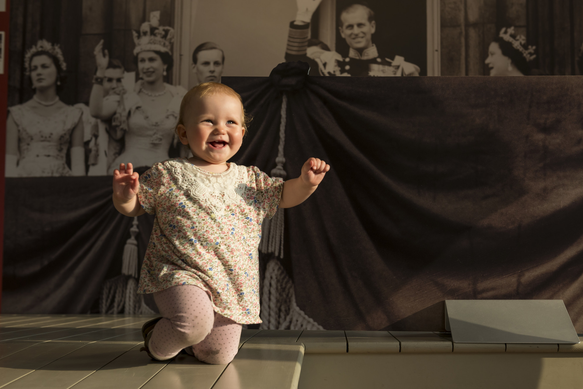Enjoy playing in the Family Pavilion! A baby is playing in the Family Pavilion, near a black and white photograph of The Queen
