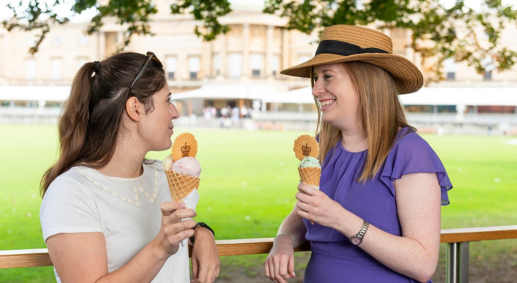 Visitors enjoying ice cream in the Palace garden. Two people holding ice creams in front of a garden