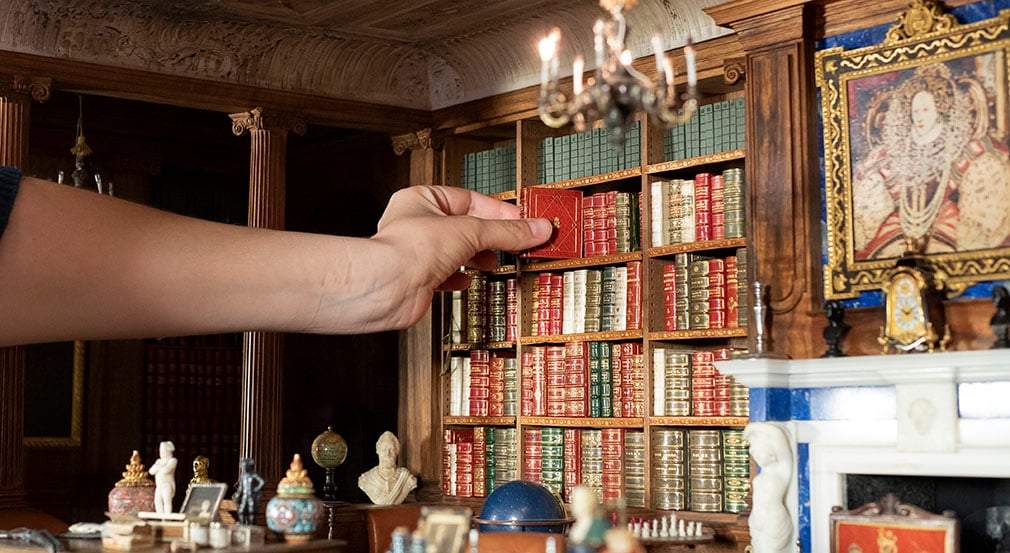 Queen Mary's Dolls' House Library. A miniature library with a hand reaching to grab a book.