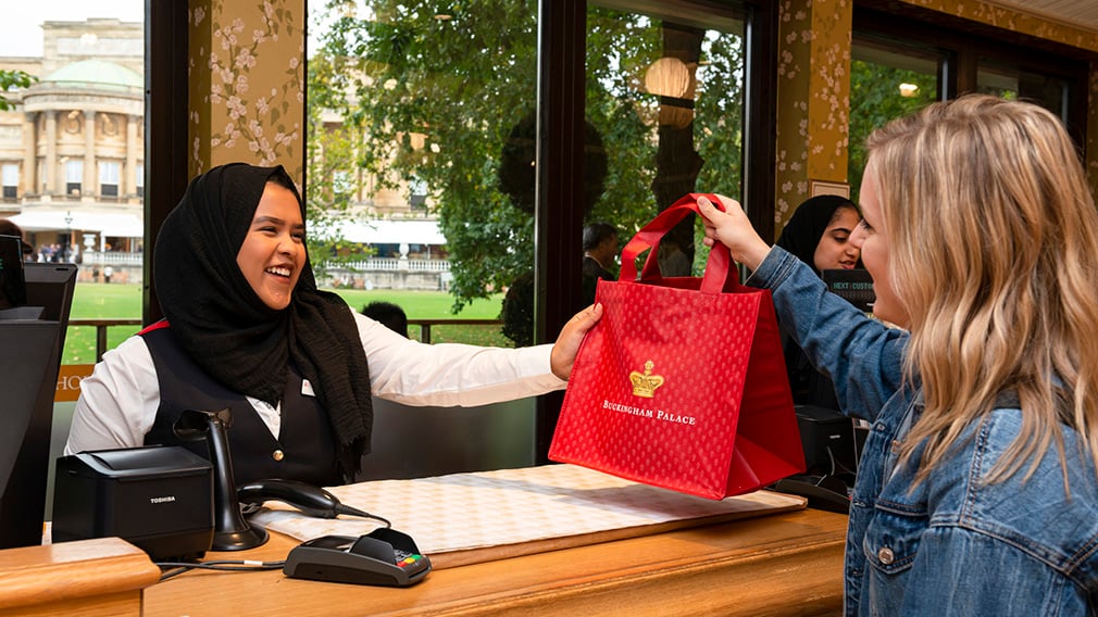 A retail assistant with a customer. A woman at a cashier desk hands a customer a red bag of her purchases
