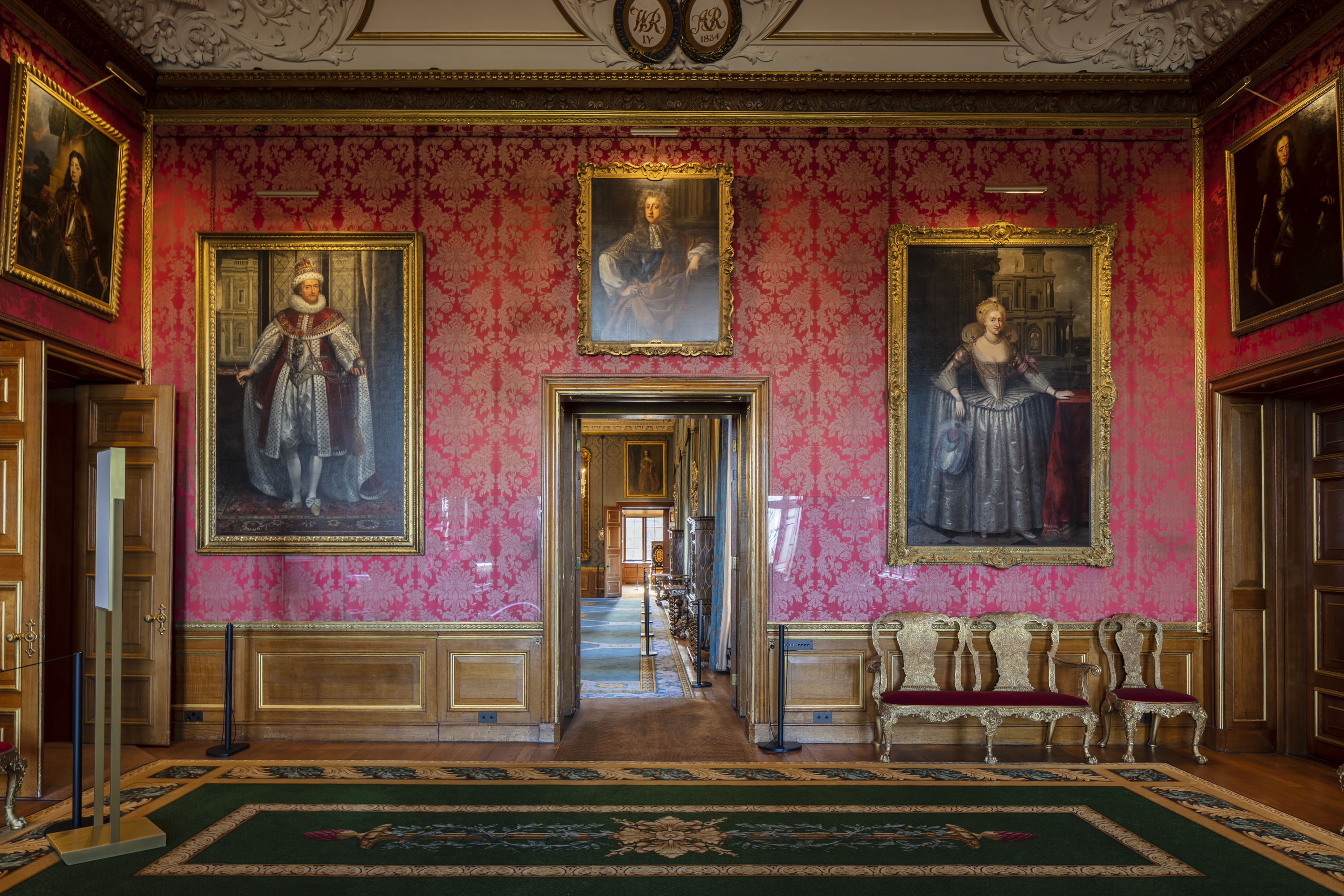 A ornate room decorated with paintings on the wall and red patterned wall paper. 