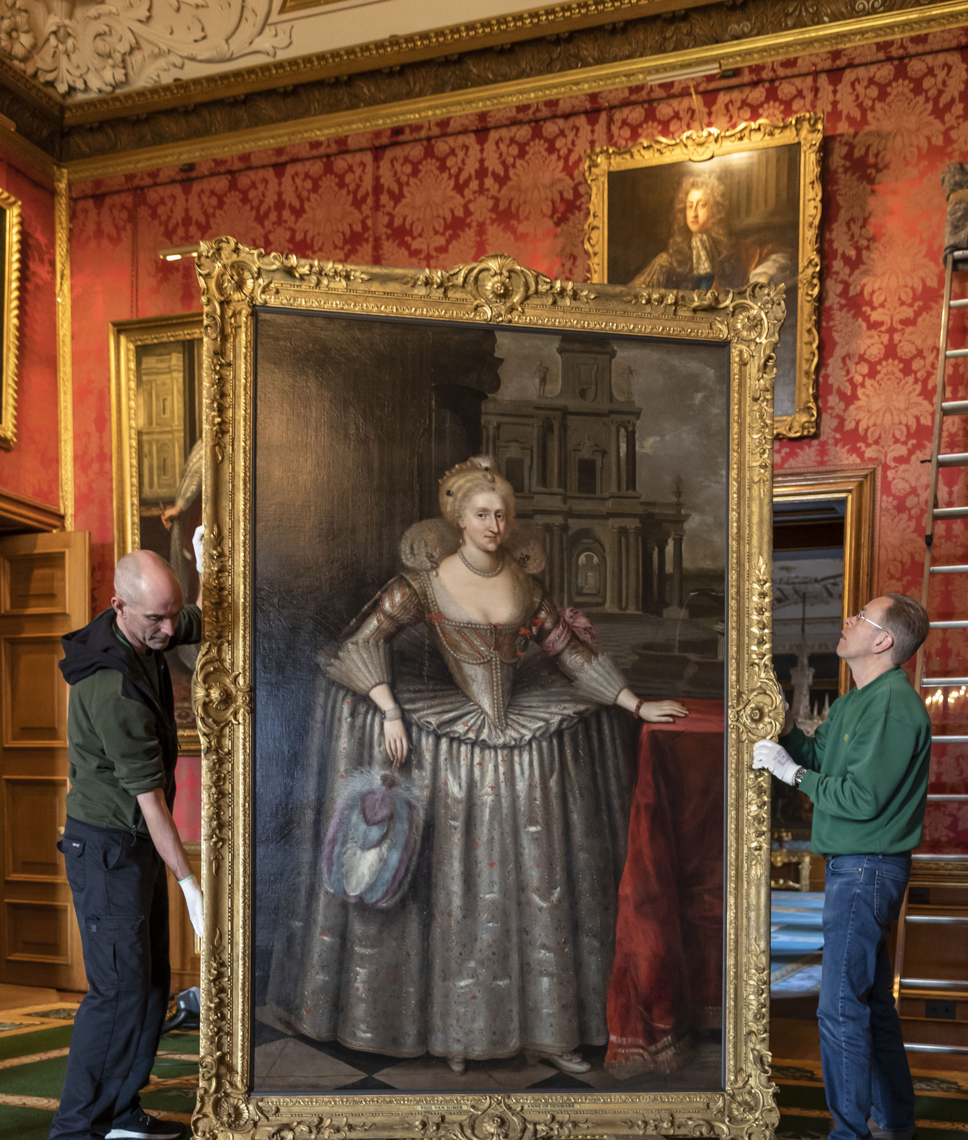 Two people holding a large painting in a gold frame. They hold a side each.