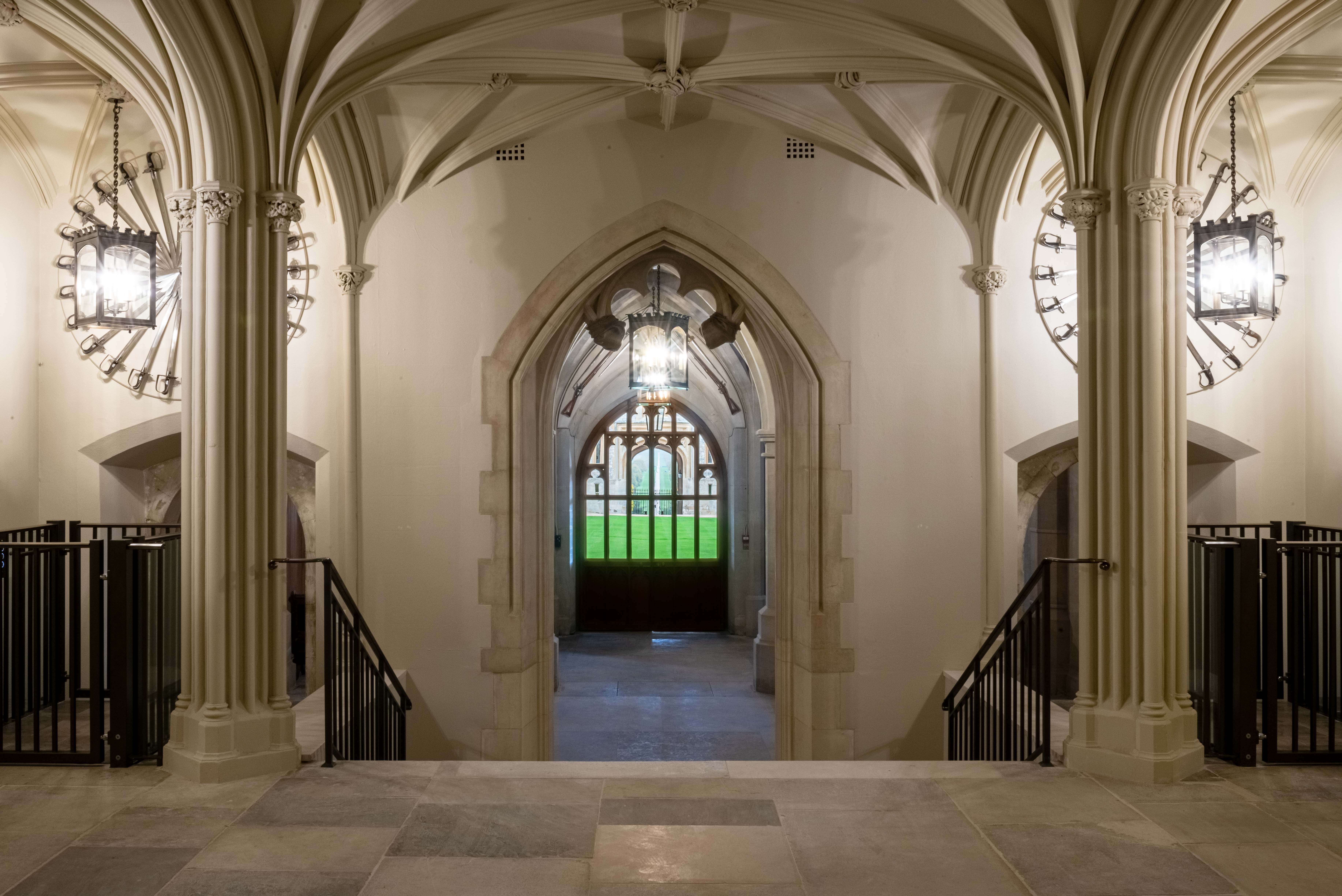 The view down to the State Entrance from the Inner Hall Image shows the Inner Hall of Windsor Catle. A large open space with stone columns.