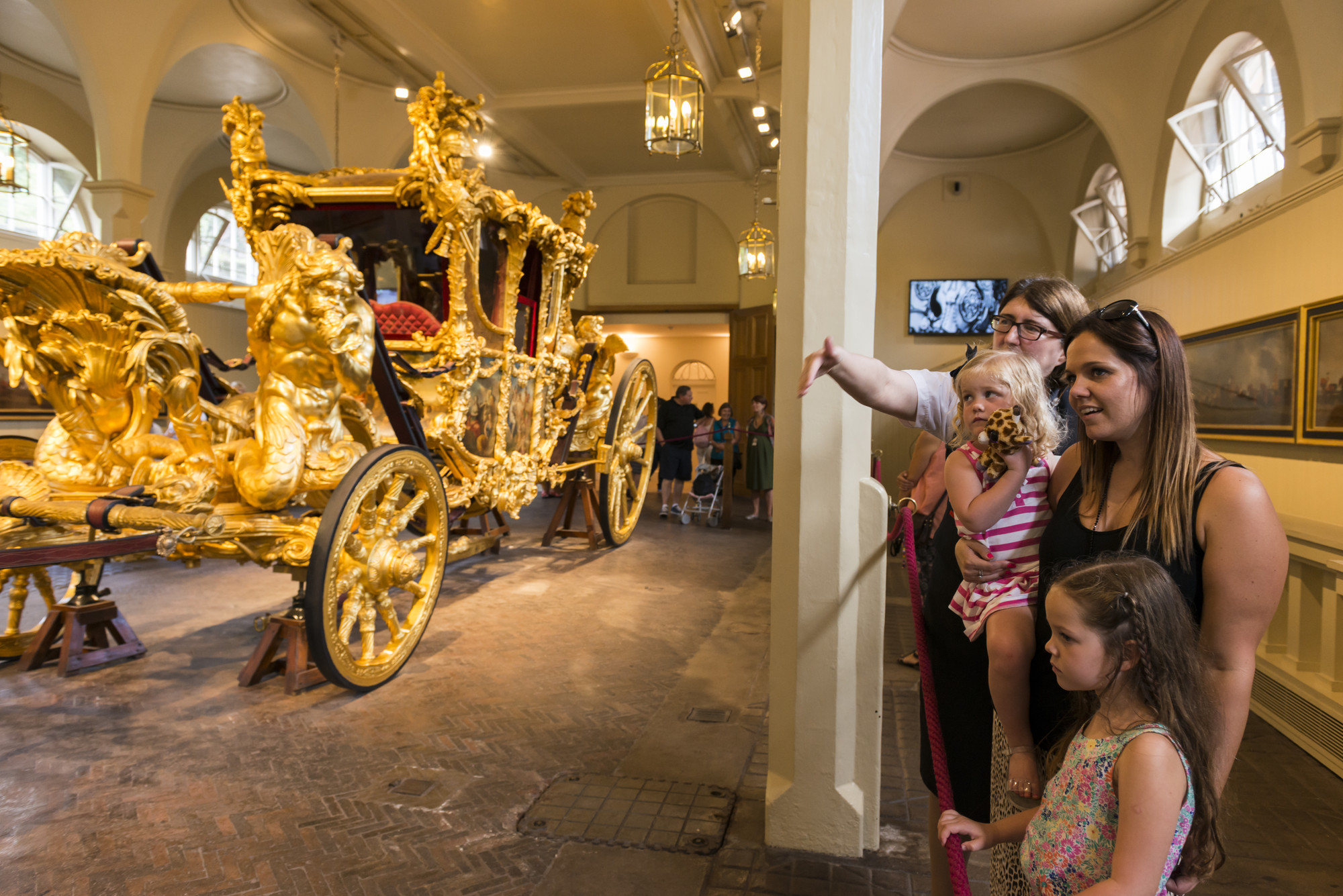 A family of a woman and two small children stand by the Gold State Coach, with the warden showing them interesting points of the Coach