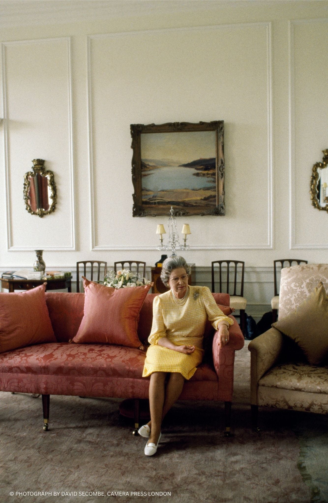 Queen Elizabeth II in the Sitting Room in the private apartments at the Palace of Holyroodhouse. Queen Elizabeth II sitting on a red sofa wearing a yellow dress.