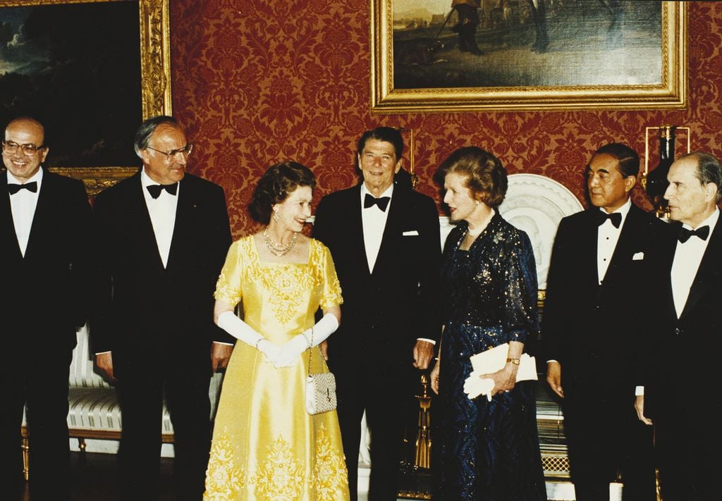 Queen Elizabeth II with a group of Heads of State in the Picture Gallery, 1984 (RCIN 2004358) Queen Elizabeth II in a yellow dresses stands with people in front of a red wall with paintings.