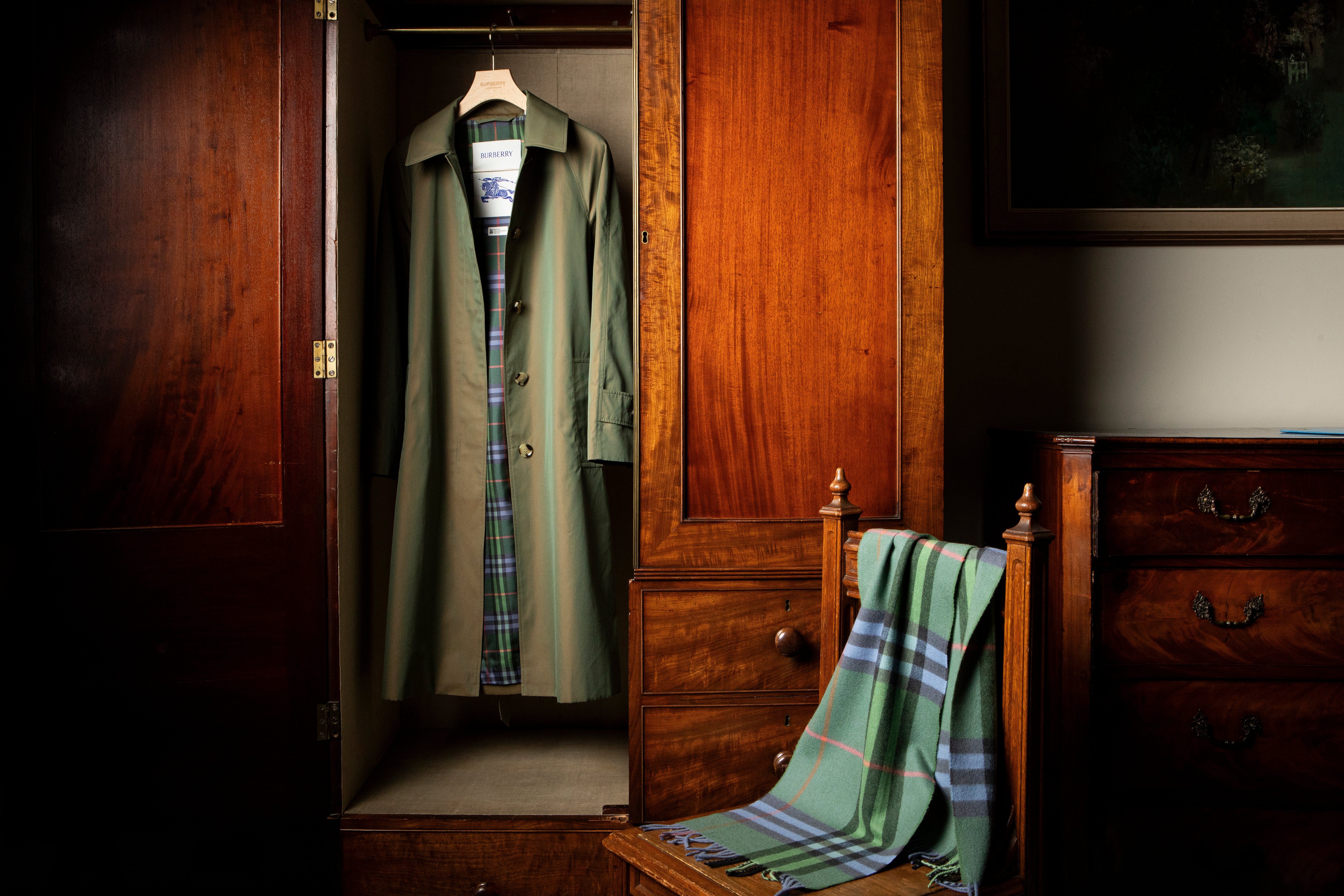 A khaki car coat hangs in wardrobe with a green and heather purple scarf draped over a chair