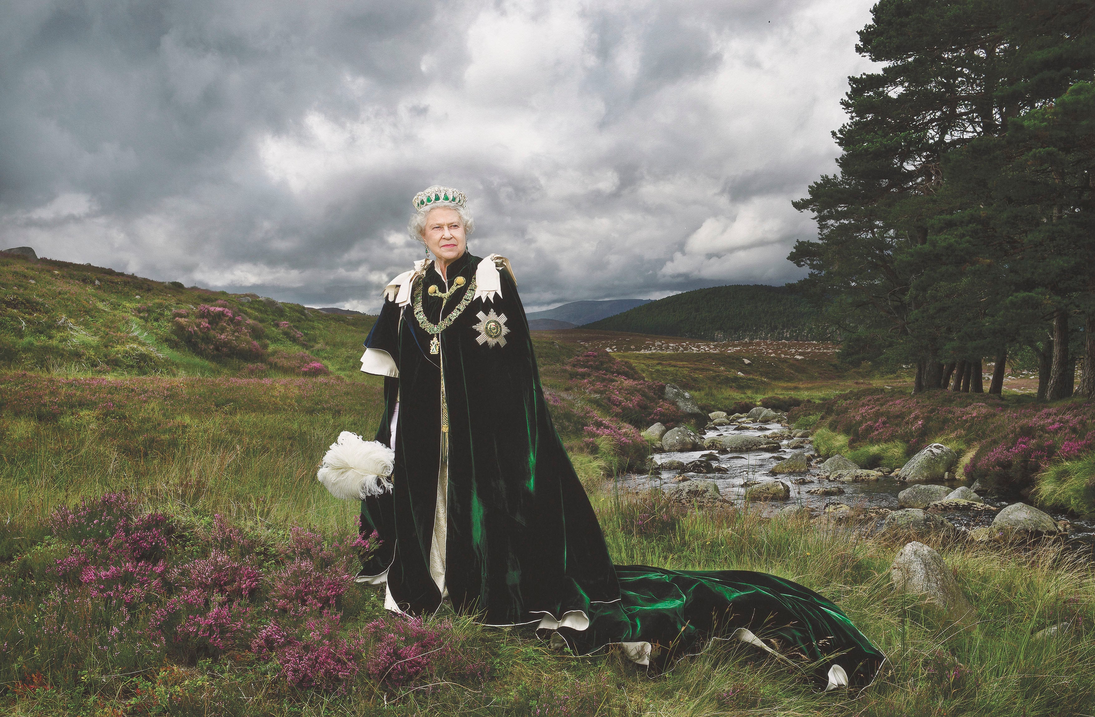 Queen Elizabeth II standing in a green cloak on a Highlands backdrop.
