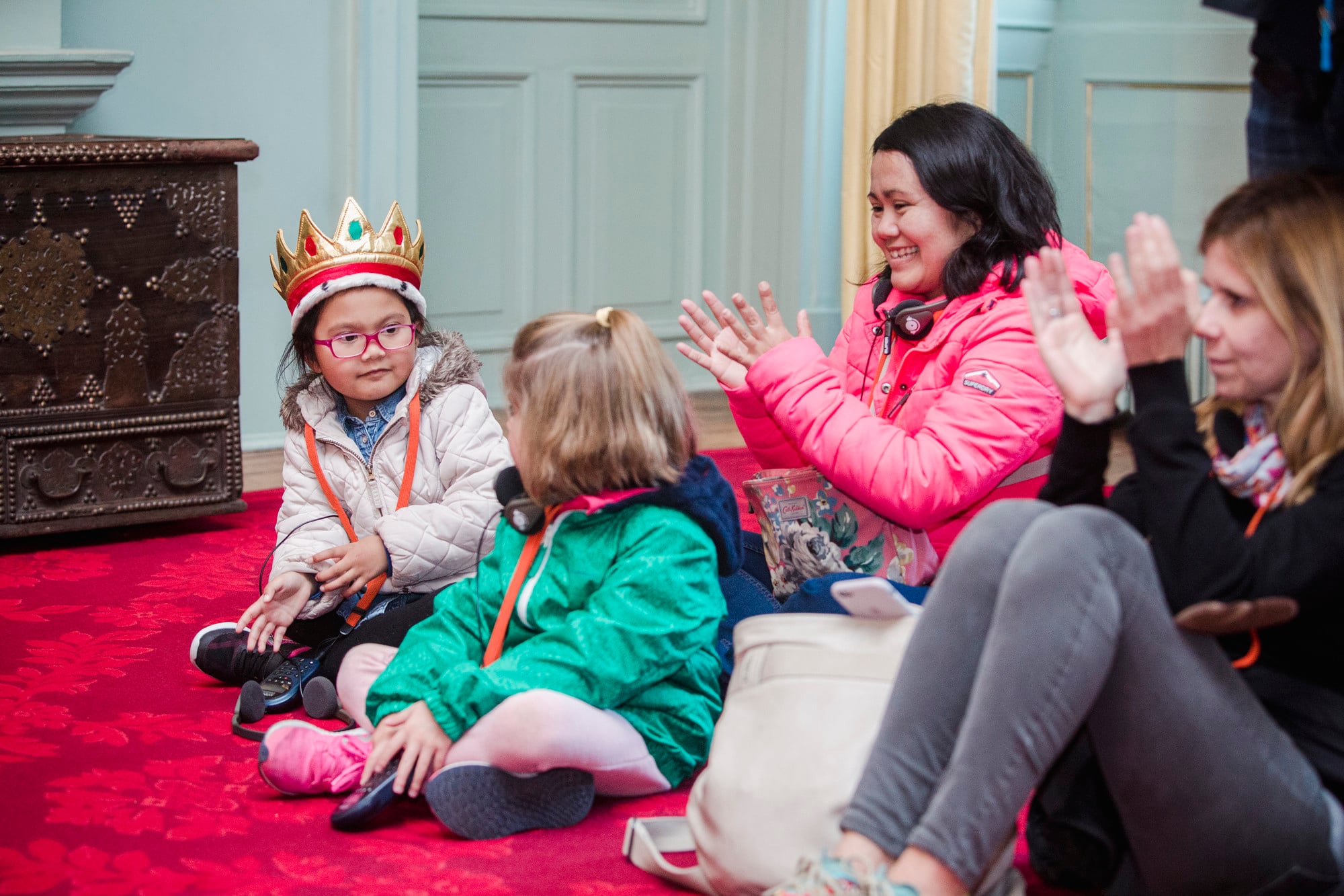 A child with a crown looks at another child, whilst adults applaud