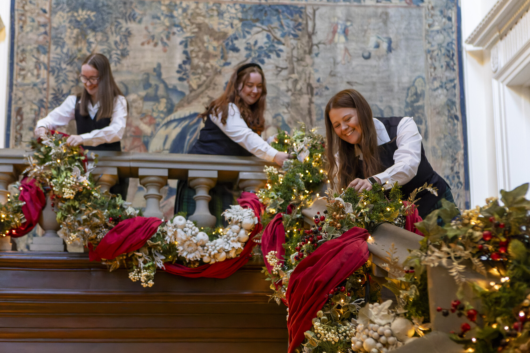 3 women arrange a Christmas garland along a staircase